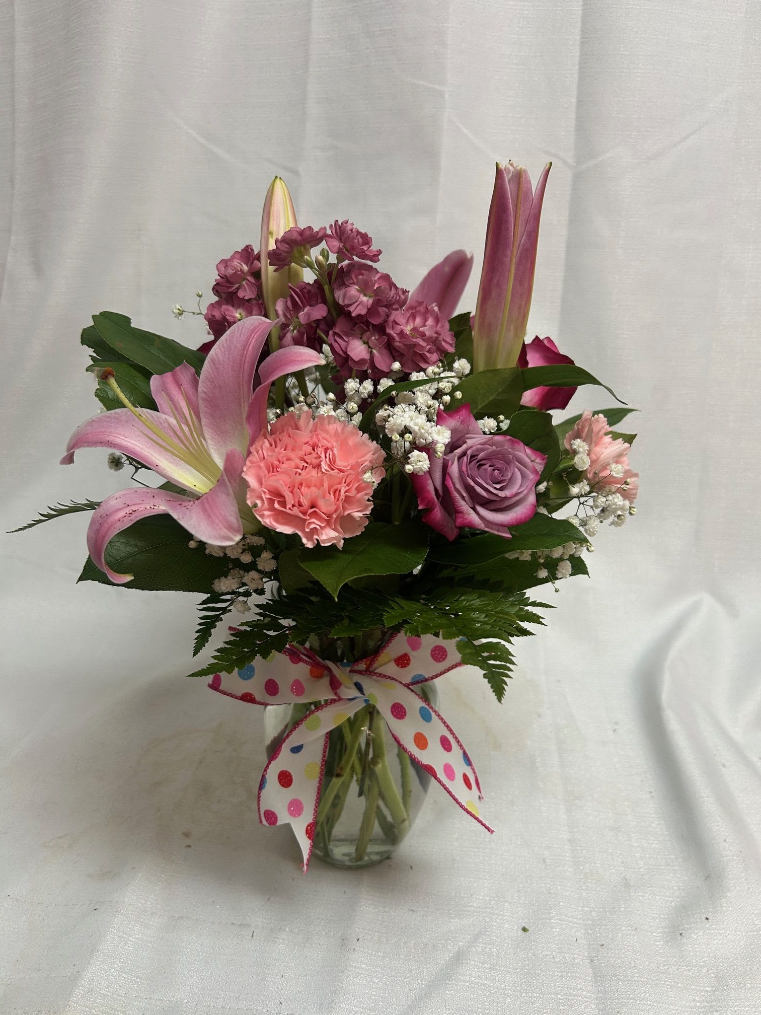 Mixed pink and purple flower arrangement in a clear vase with a polka dot bow