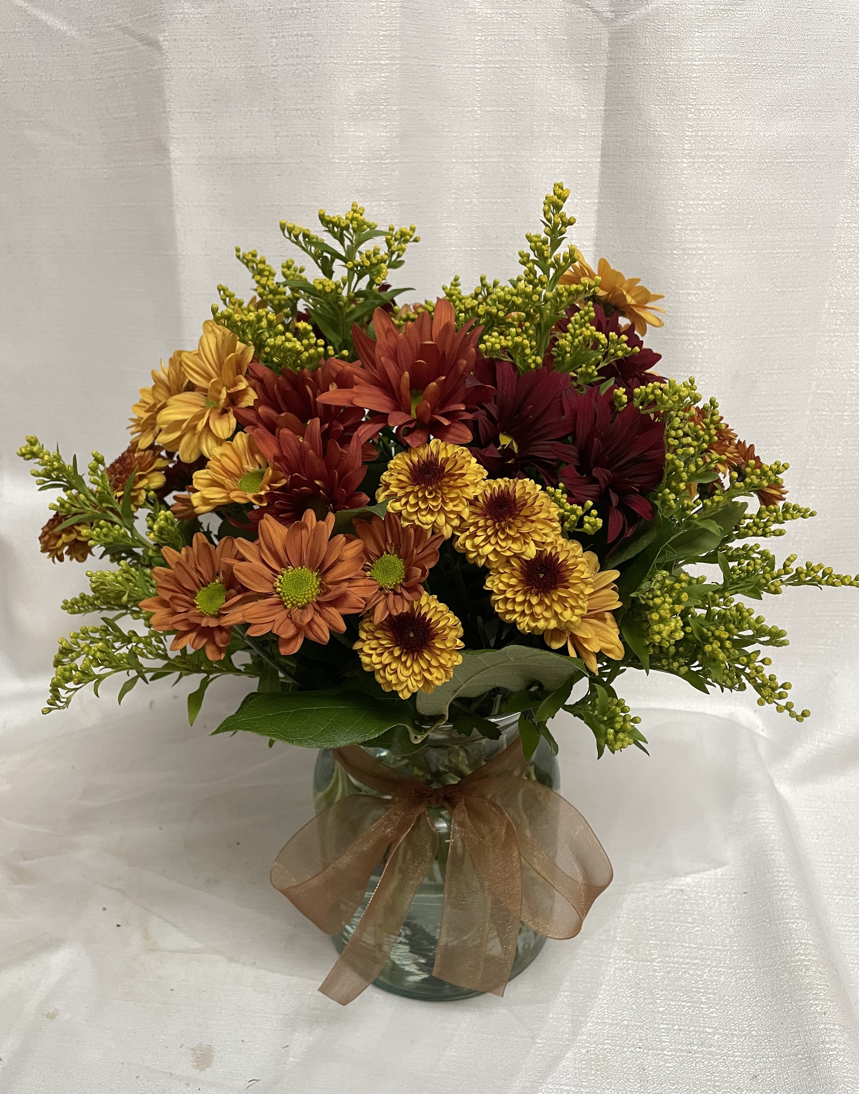 Autumn bouquet of orange, yellow, and burgundy flowers in a glass vase