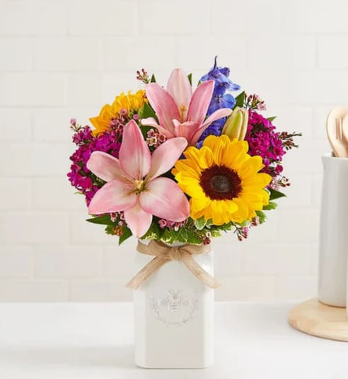 Bouquet of pink lilies and yellow sunflowers in a white vase