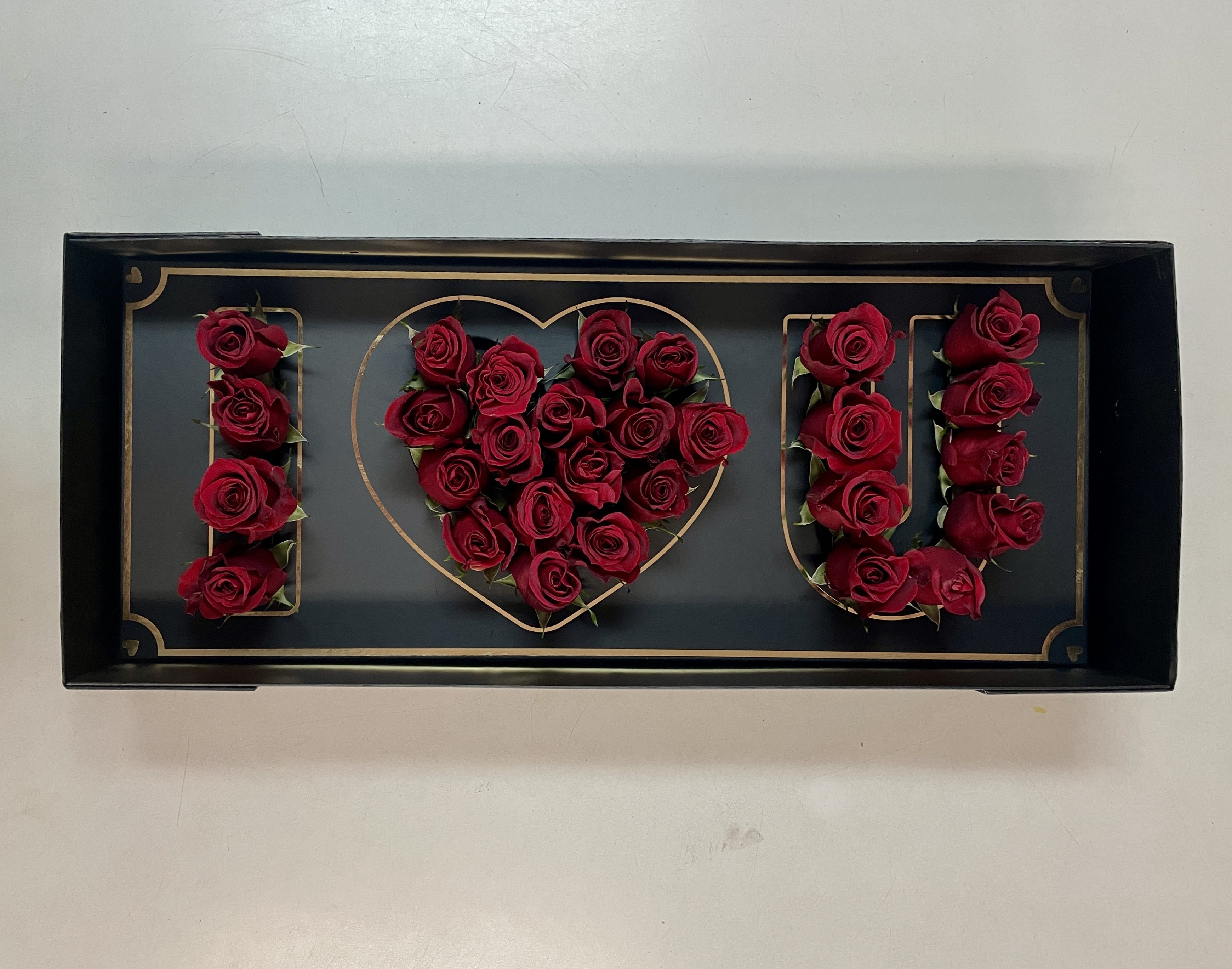Red roses arranged to spell "I ♥ U" in a black tray