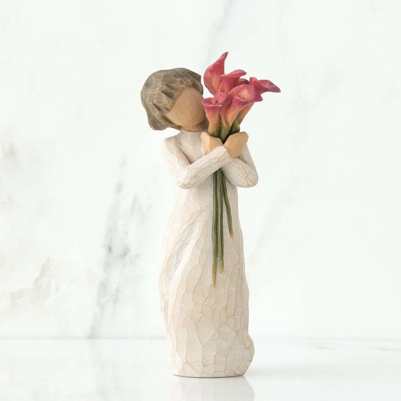 Bloom - A sculptural keepsake that feels like a quiet, heartfelt gift-this calla lily figurine arrangement is perfect as a sympathy tribute or a thoughtful "thinking of you" present. The small decorative figure holds a cluster of pink calla lilies, making the piece both a mini flower arrangement and a lasting memento for anniversaries of loss, a bedside remembrance, or a gentle get-well gesture.  Hand-carved in a muted white and beige finish, the figure's long textured dress contrasts beautifully with the vivid pink calla lilies for a soft, contemplative look. Compact in scale, the design reads more like a keepsake than a traditional bouquet, so it fits neatly on a mantel, nightstand, or desk without taking up much space. Includes the sculptural hard good with the arranged flowers ready to display.  Designed to comfort and to be displayed, this piece makes the recipient feel seen and remembered-an understated way to say you care. Because it's a decorative object with preserved or artful flowers, place it away from direct sunlight to preserve color; perfect for immediate delivery as a meaningful gift that will be cherished.