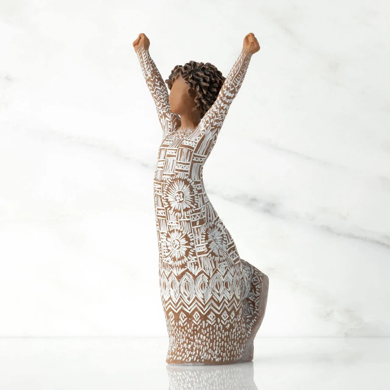 Willow Tree Courageous Joy - A hand-carved, sculptural figurine captures the spirit of celebration in this keepsake arrangement-perfect as a sympathy comfort piece or a thoughtful gift to mark a milestone. The Willow Tree Courageous Joy sculpture stands with arms lifted in an expression of uplifted strength, making it a meaningful choice for moments when you want the recipient to feel seen, supported, and quietly celebrated.  The piece features a warm brown base tone with delicate white etched patterns across the dress and body that emphasize texture and handcrafted detail. Though shown alone as a decorative art object, it pairs beautifully with white flowers or neutral-toned arrangements to create a serene display for a mantel, bedside table, or memorial space. Its artisan look makes it feel personal and enduring-an object the recipient can place where it will offer comfort and daily reminder of your care.  Ideal for offering sympathy, encouragement after a loss, or congratulating someone on a personal achievement, this figurine communicates empathy and joyful resilience without words. Lightweight and easy to place, it arrives ready to be gifted as a lasting memento; consider adding a simple bouquet in white tones to complete the presentation.