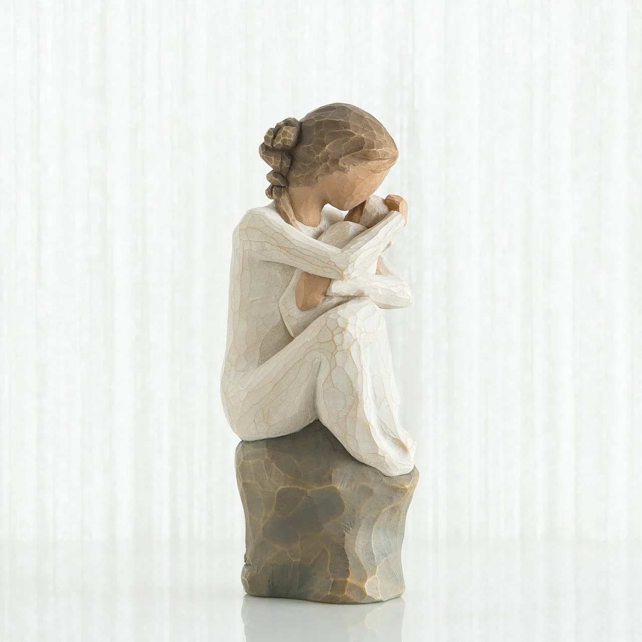 Willow Tree Guardian - A quietly contemplative carved figurine in soft cream and taupe tones, this flower arrangement-style piece - ideal for sympathy or remembrance - brings a sense of calm to any memorial or thoughtful-gift moment. The seated girl with her head bowed and arms wrapped around herself creates an immediate emotional connection; for someone grieving or in need of comfort, this sculpture-vignette reads as a gentle, respectful way to say you're thinking of them.  The hand-carved look and textured finish give the figurine an artisan feel, and it rests on a rough, stone-like base that makes the whole composition feel sculptural and durable rather than fleeting. Subtle neutral colors-soft white, cream and taupe-allow it to blend with home décor or a memorial display without competing with accompanying flowers or candles.  Perfect for placing on a mantel, bedside table, or memorial shelf, the piece offers a lasting token of sympathy that the recipient can return to again and again. Its compact, decorative scale makes it easy to pair with fresh flowers or greenery if desired; no special care is required beyond gentle dusting to preserve the textured finish.