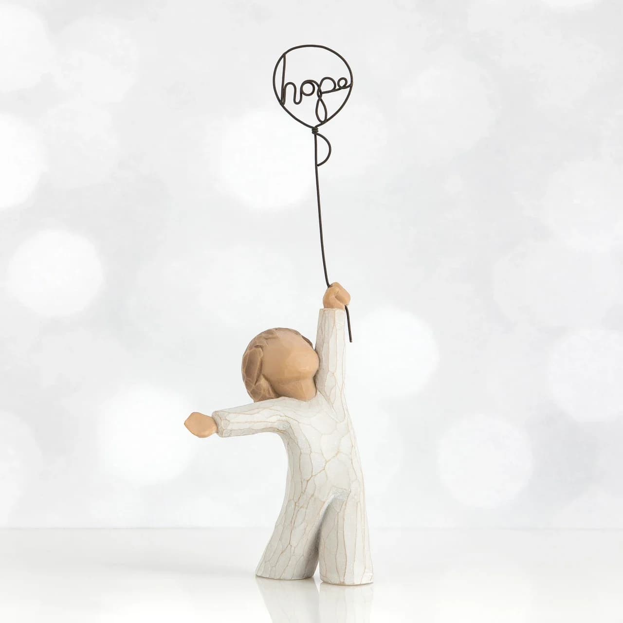 Willow Tree Hope - A pale, handmade-feeling keepsake that speaks to comfort and encouragement, this Willow Tree Hope piece is a thoughtful sympathy or encouragement gift. The small figurine of a child-like figure holds a wire balloon shaped into the word "hope," making it an understated way to say "I'm thinking of you" or "you are not alone" for moments of loss, recovery, or quiet support.  Finished in a soft white and beige crackle texture, the neutral palette and rustic surface create a calming, sentimental presence that fits on a bedside table, mantel, or desk. Because it is presented as a decorative figurine with a wire balloon topper rather than a floral display, it functions as a lasting keepsake the recipient can return to long after flowers have faded - a gentle reminder of care and hope. Care: dust gently with a soft cloth; keep out of direct moisture.