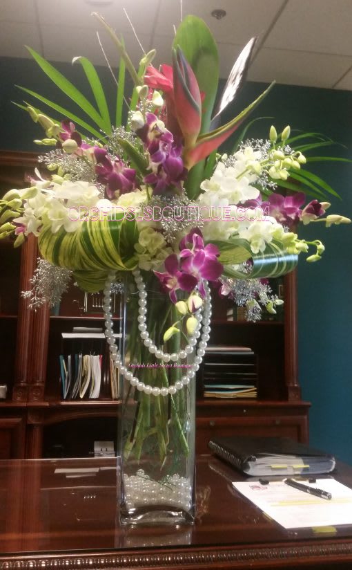 Tall orchid arrangement in a clear glass vase with pearl strands