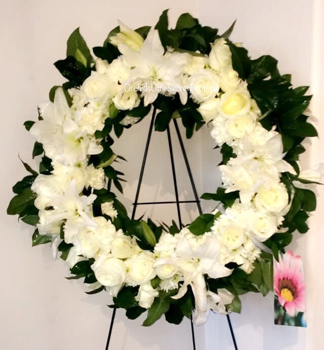 White floral wreath on a black stand with dark green leaves