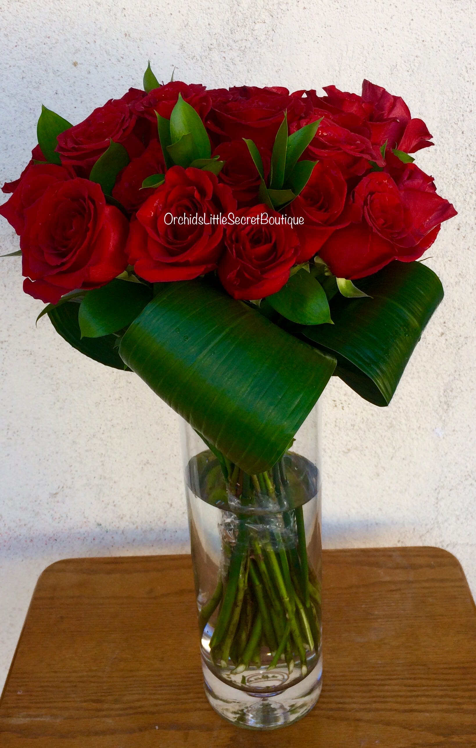Red roses arranged in a clear glass vase with broad green leaves