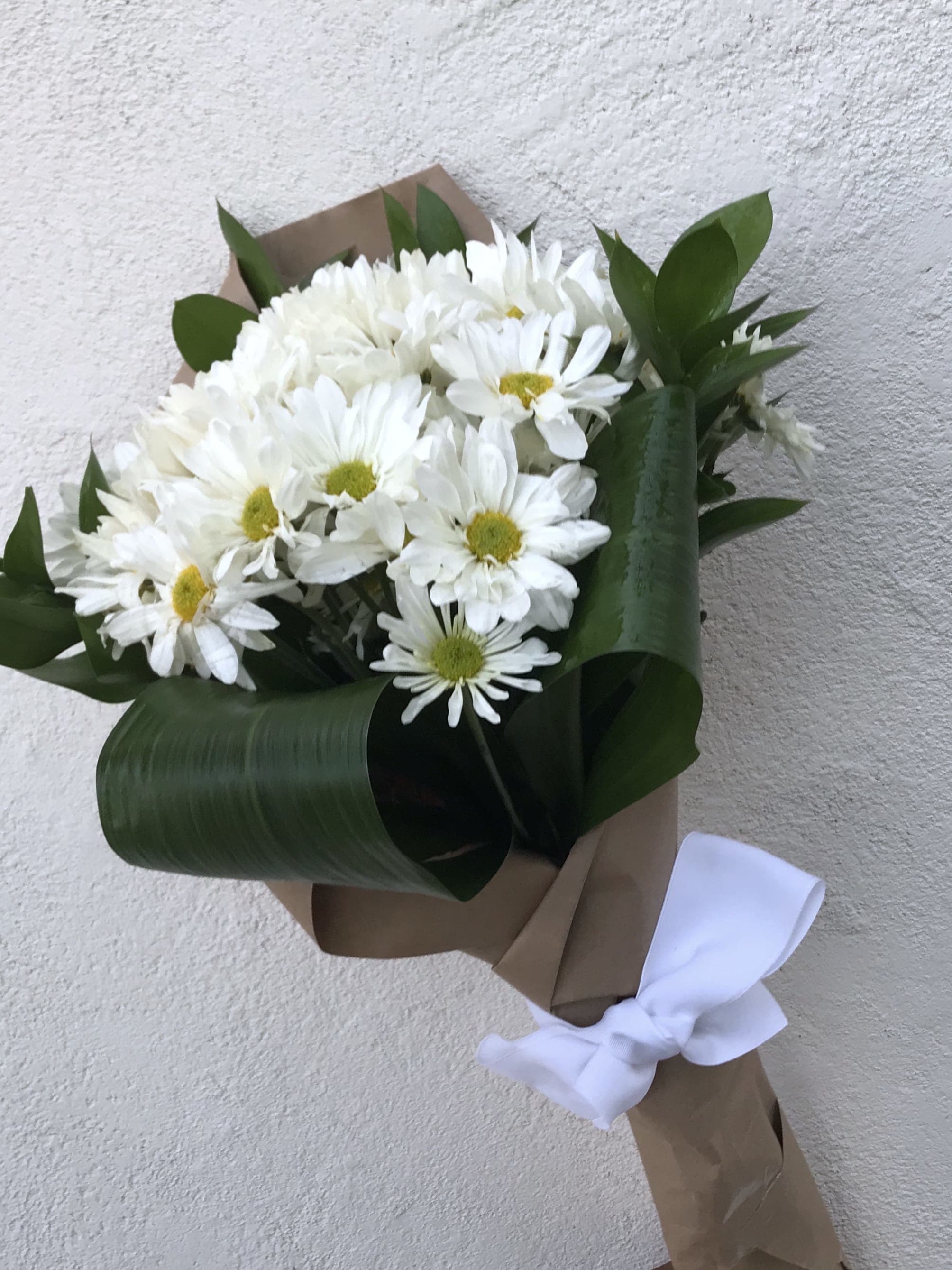 Bouquet of white daisies wrapped in brown paper with a white ribbon