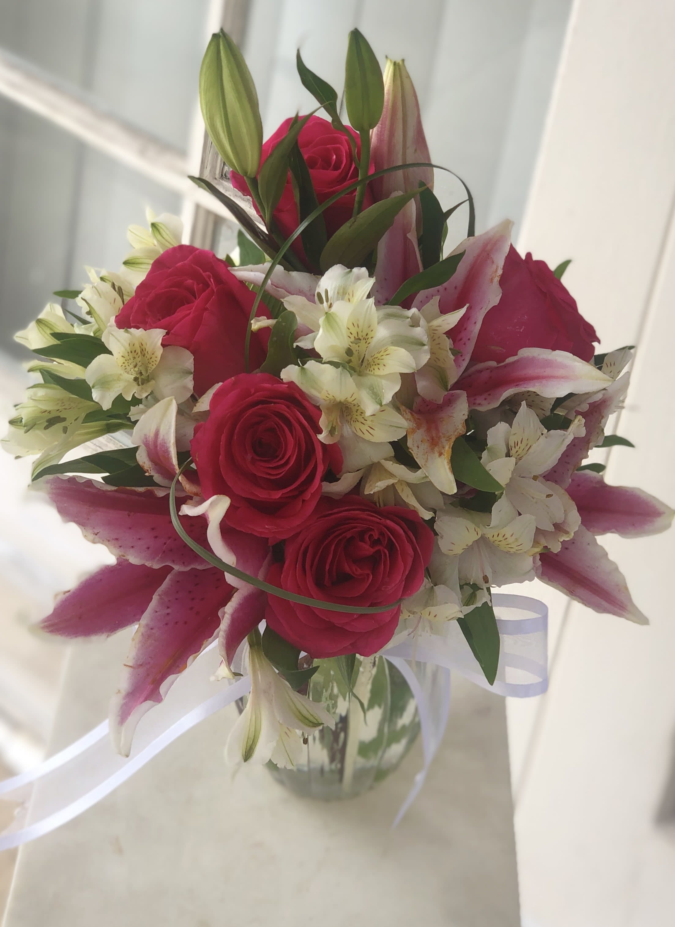 Bouquet of pink roses and lilies in a glass vase with white ribbon