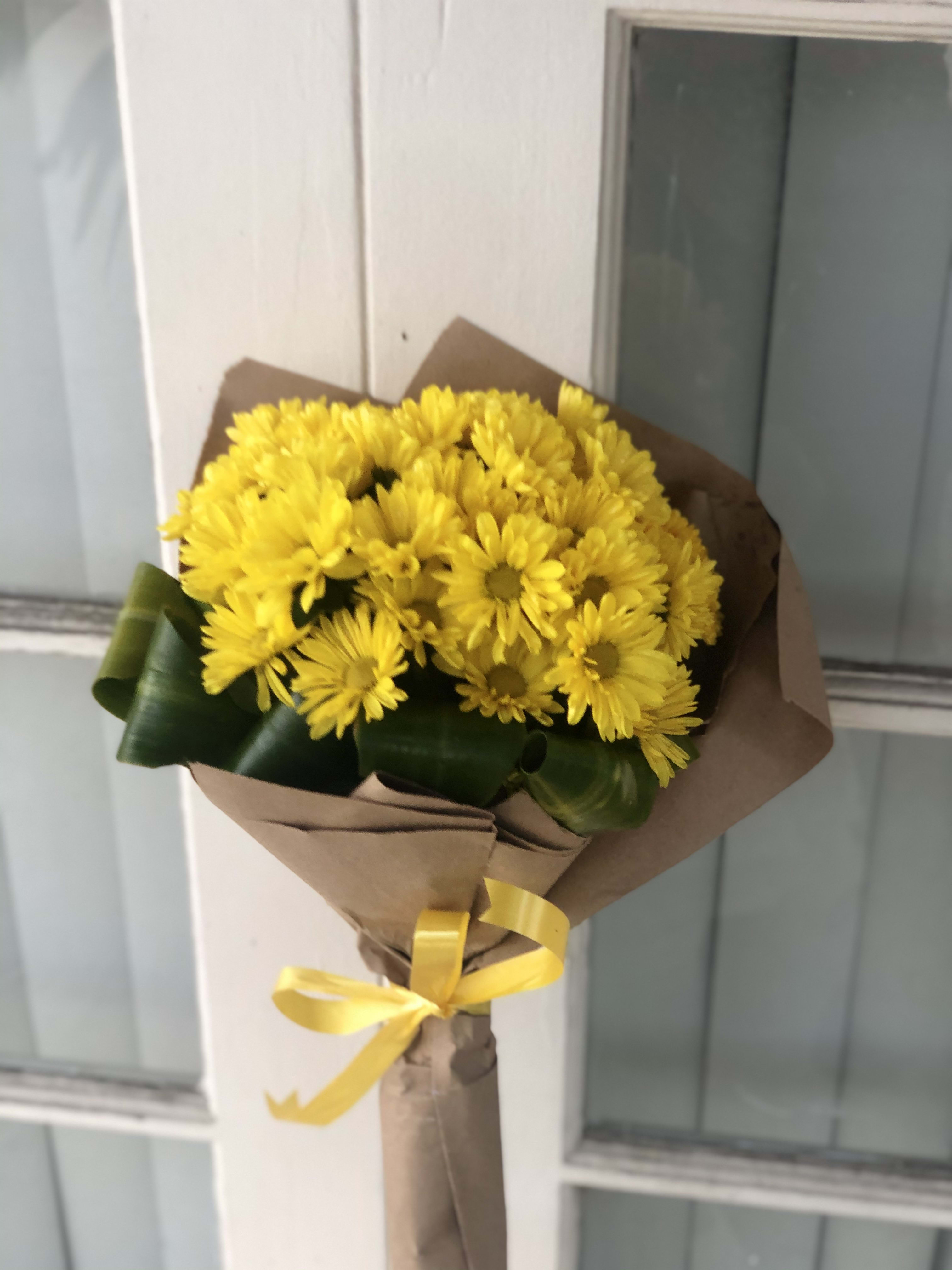 Bouquet of yellow daisies wrapped in brown paper with a yellow ribbon