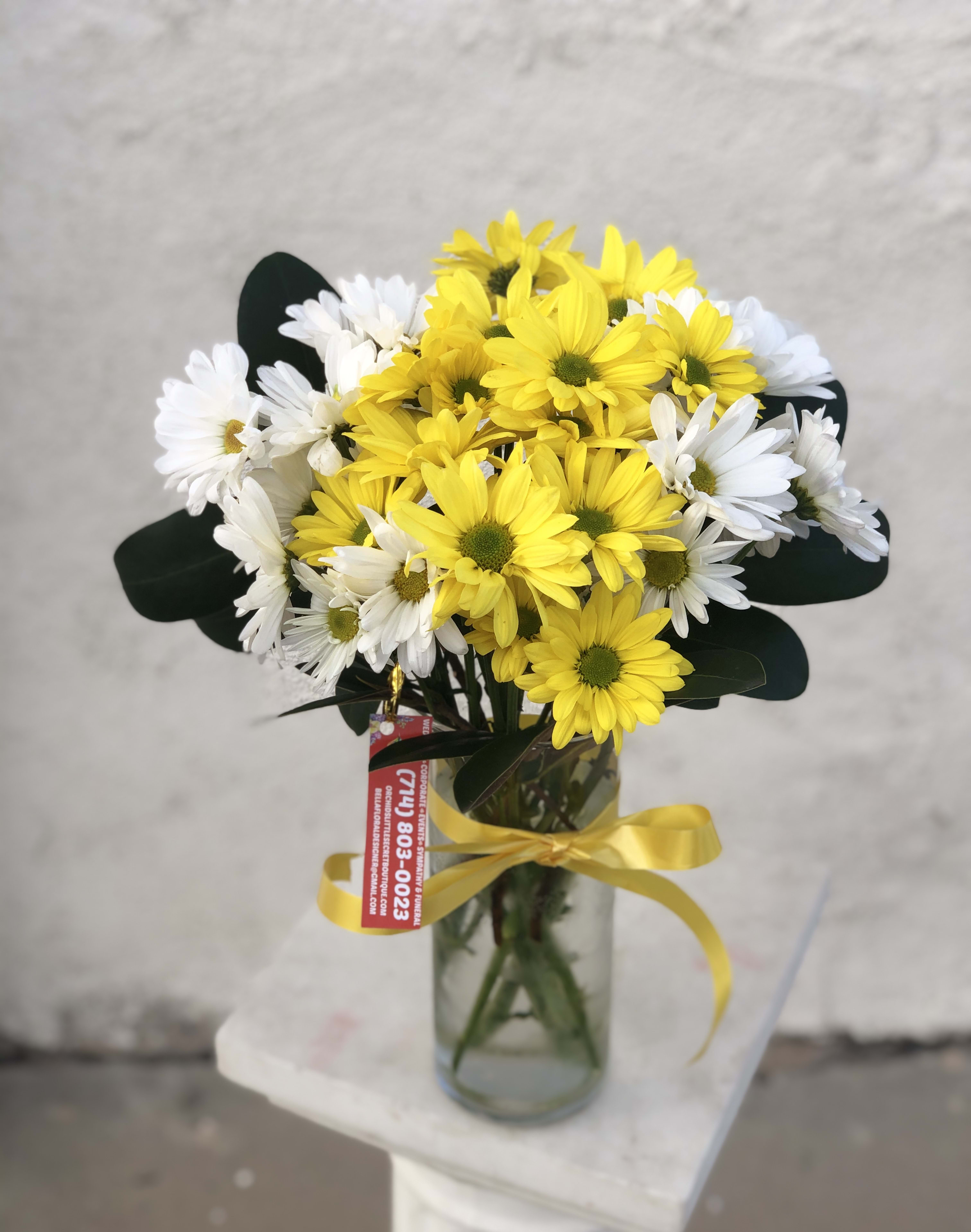 Bouquet of yellow and white daisies in a glass vase with a yellow ribbon