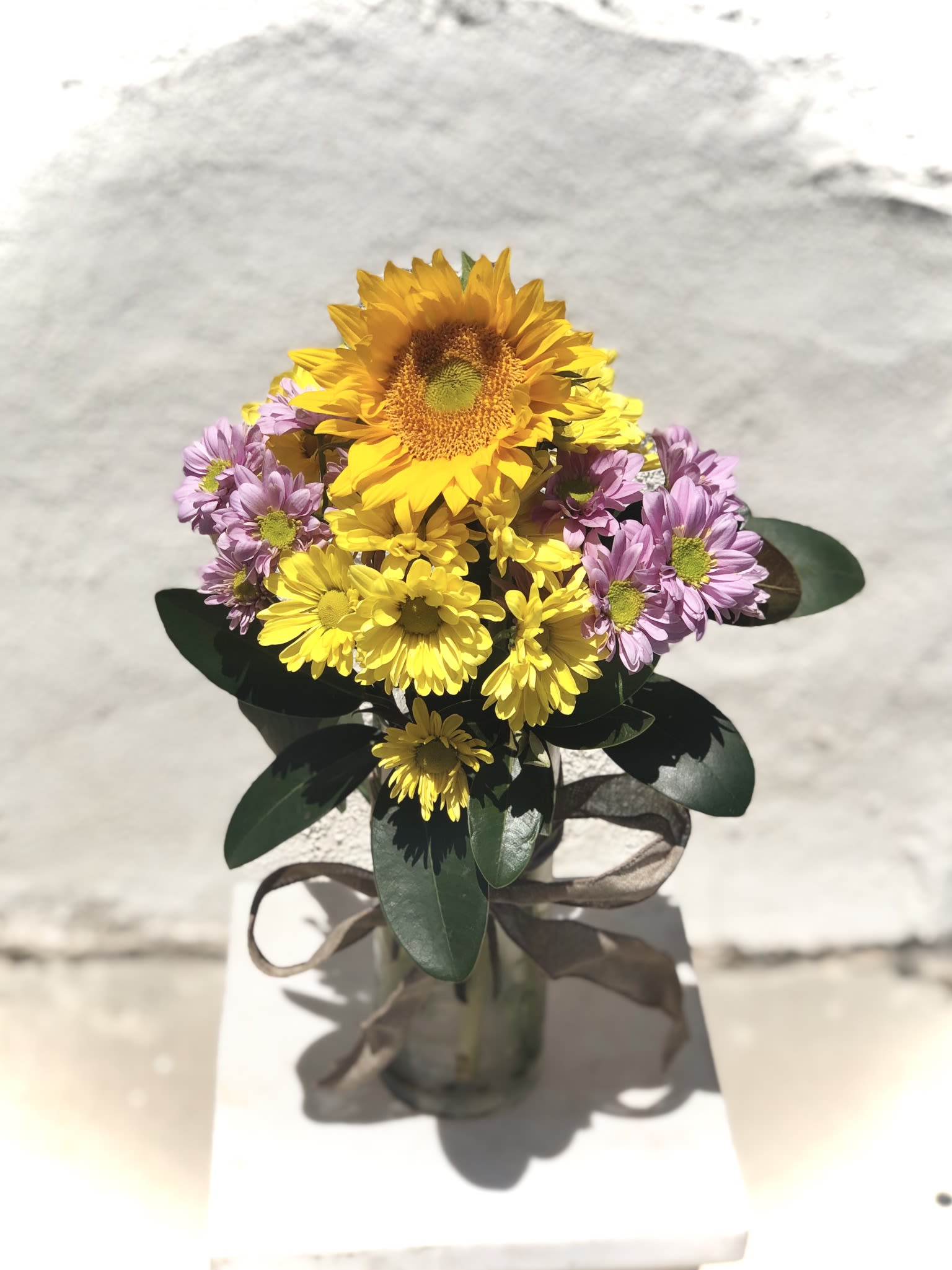 Bouquet of yellow sunflowers and purple daisies in a glass vase
