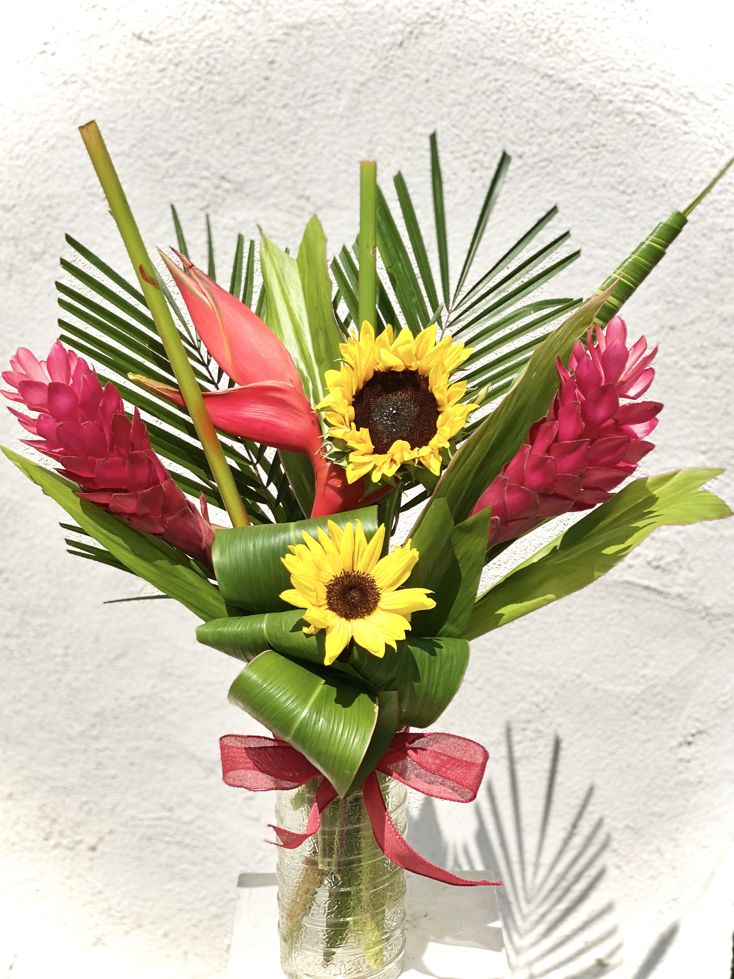 Tropical bouquet with sunflowers and pink ginger in a glass vase