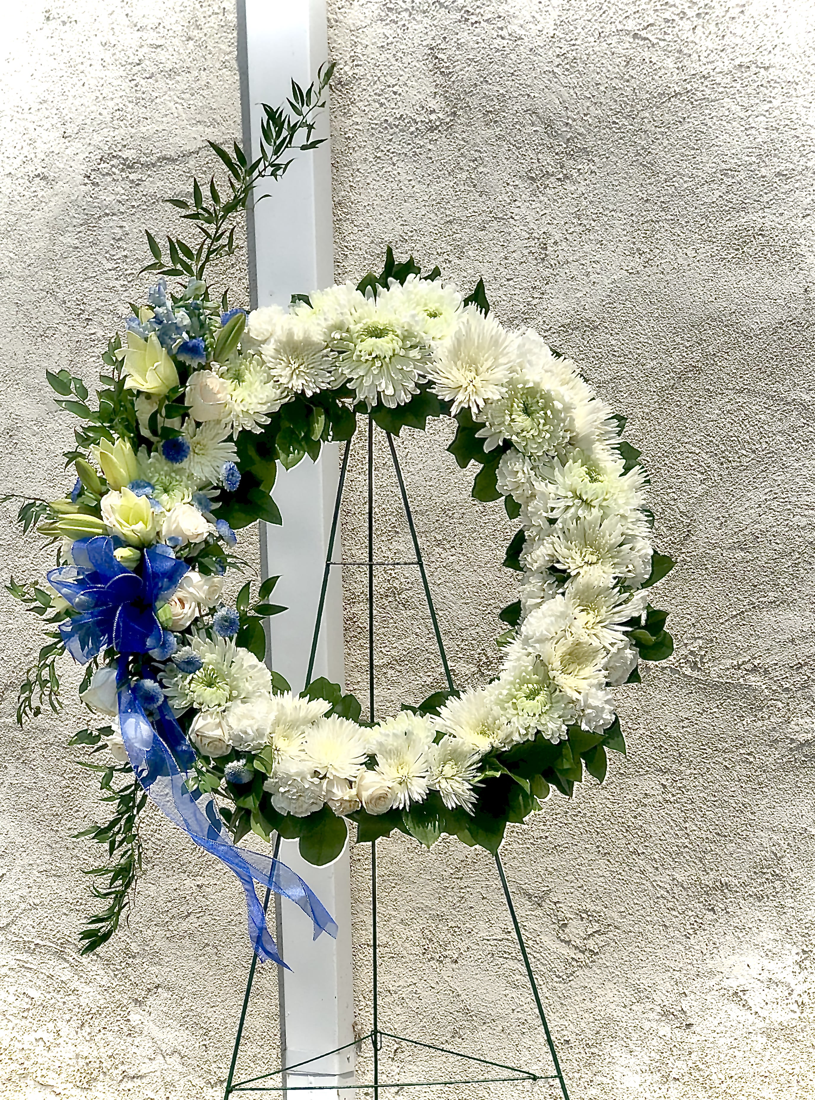White floral wreath on a stand with blue ribbon accents
