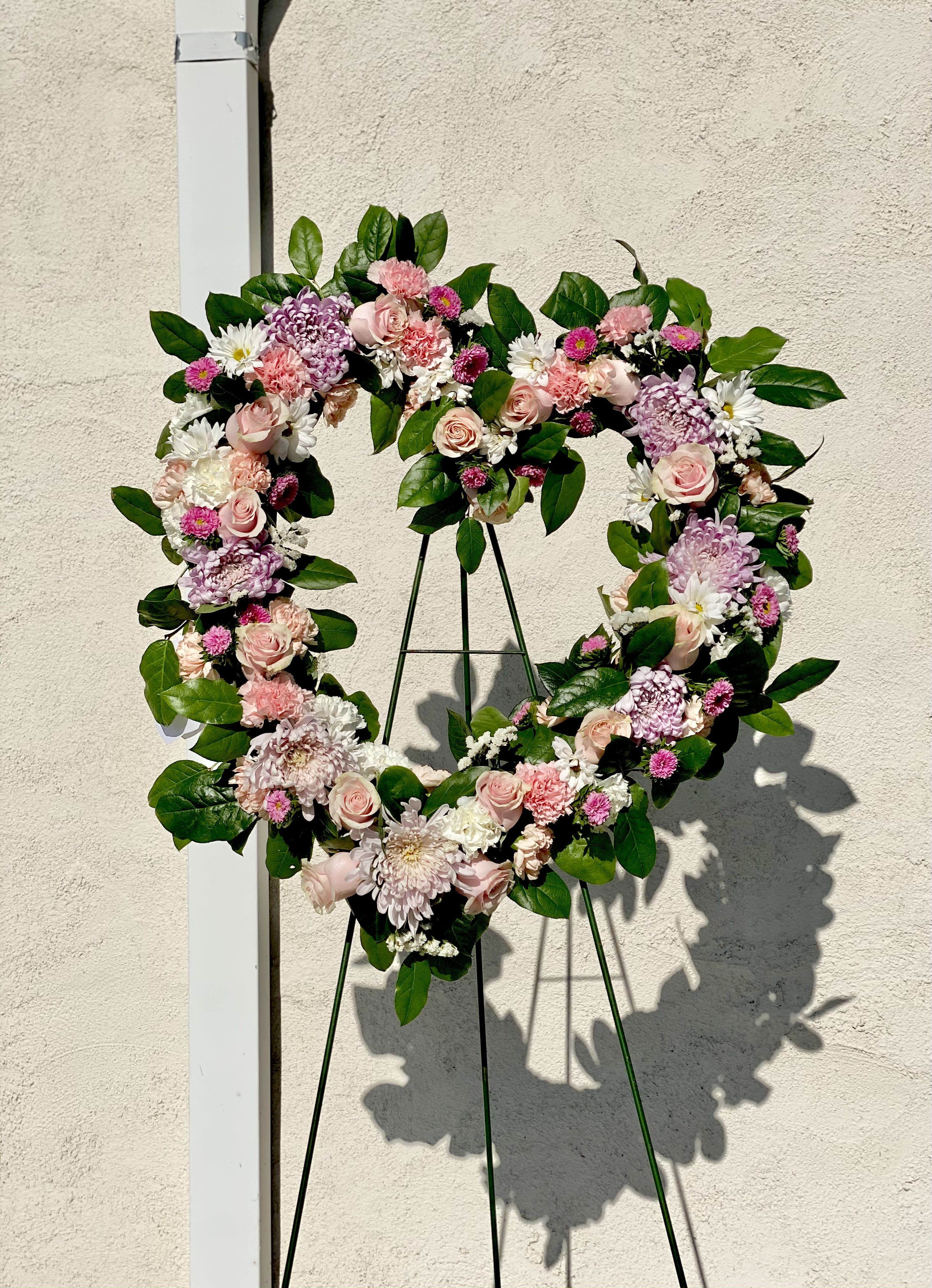 Heart-shaped floral wreath with pink and white flowers on a stand