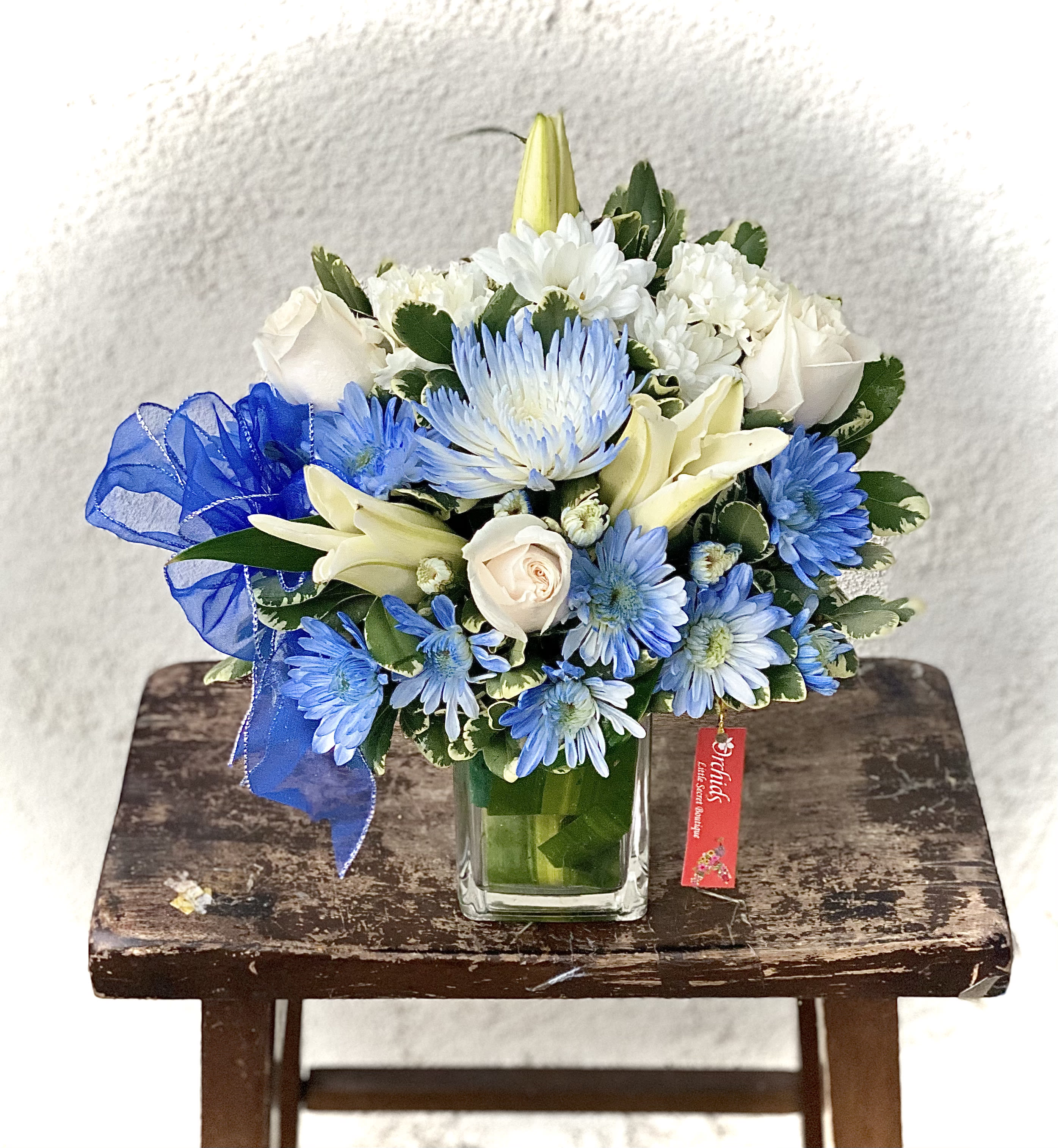 Blue and white mixed bouquet in a square glass vase with a ribbon