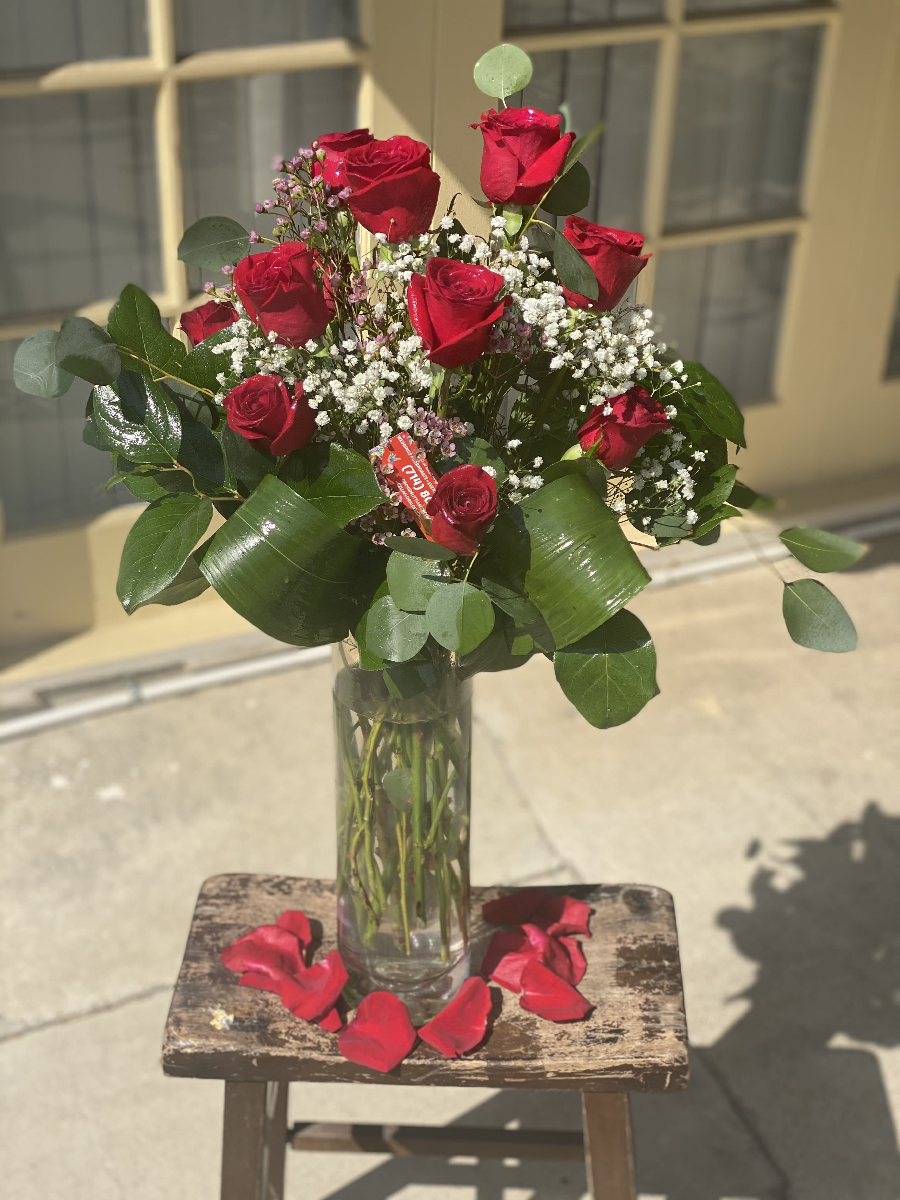 Red roses in a clear glass vase with baby's breath and rose petals