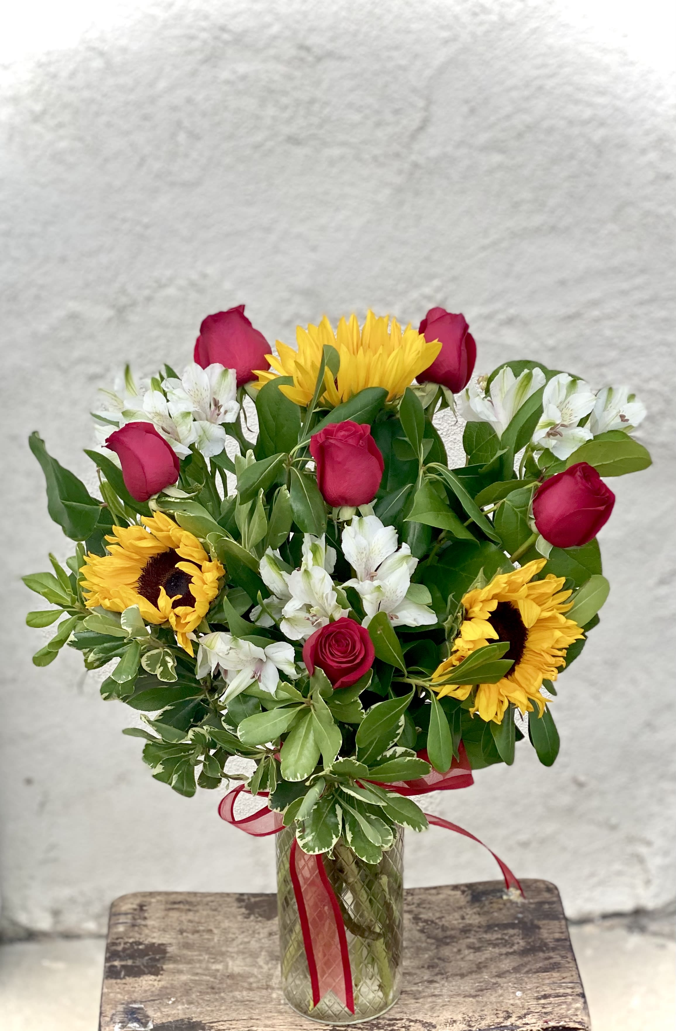 Bouquet of red roses, sunflowers, and white alstroemeria in a glass vase