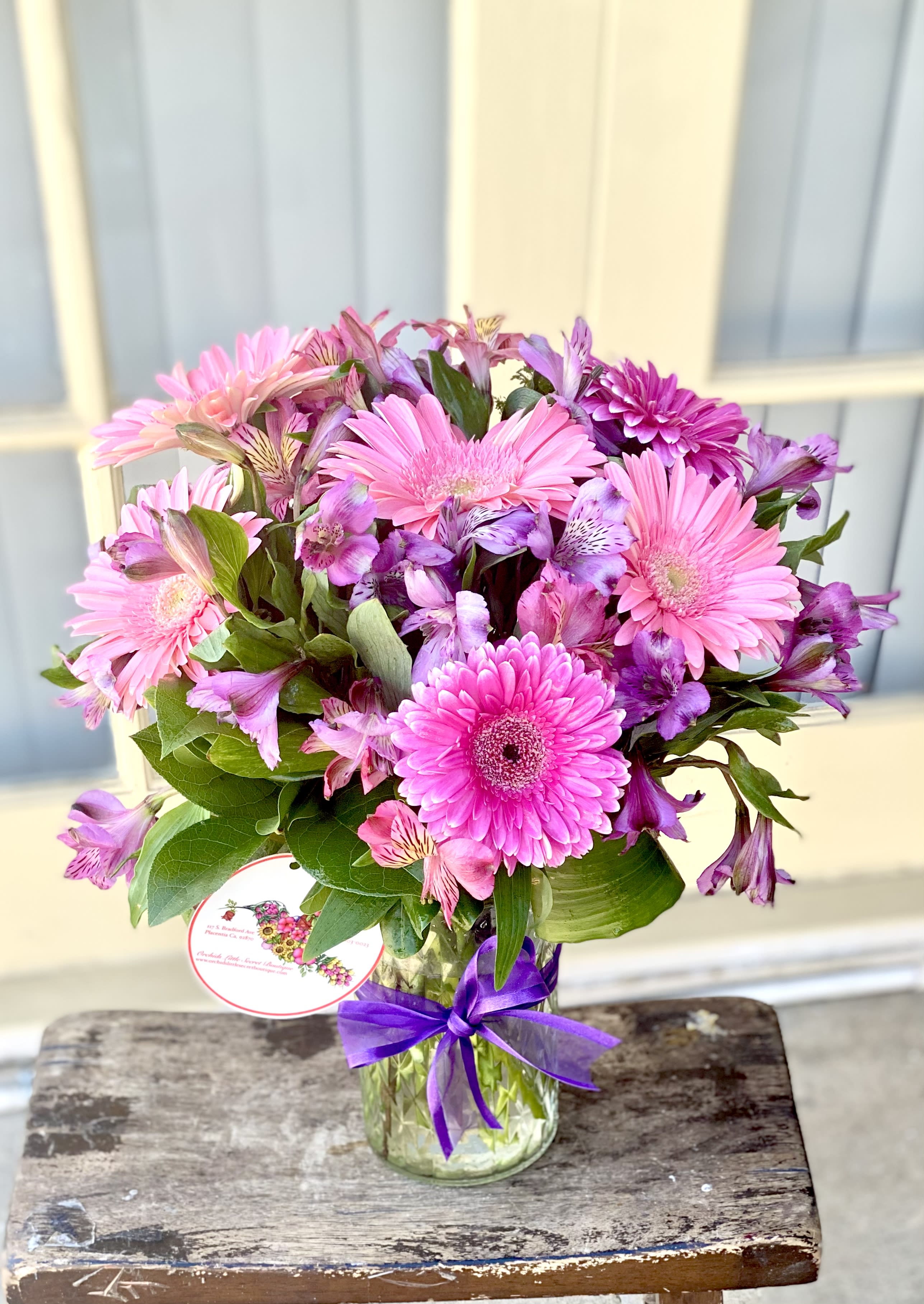 Pink and purple mixed bouquet in a glass vase with a purple ribbon
