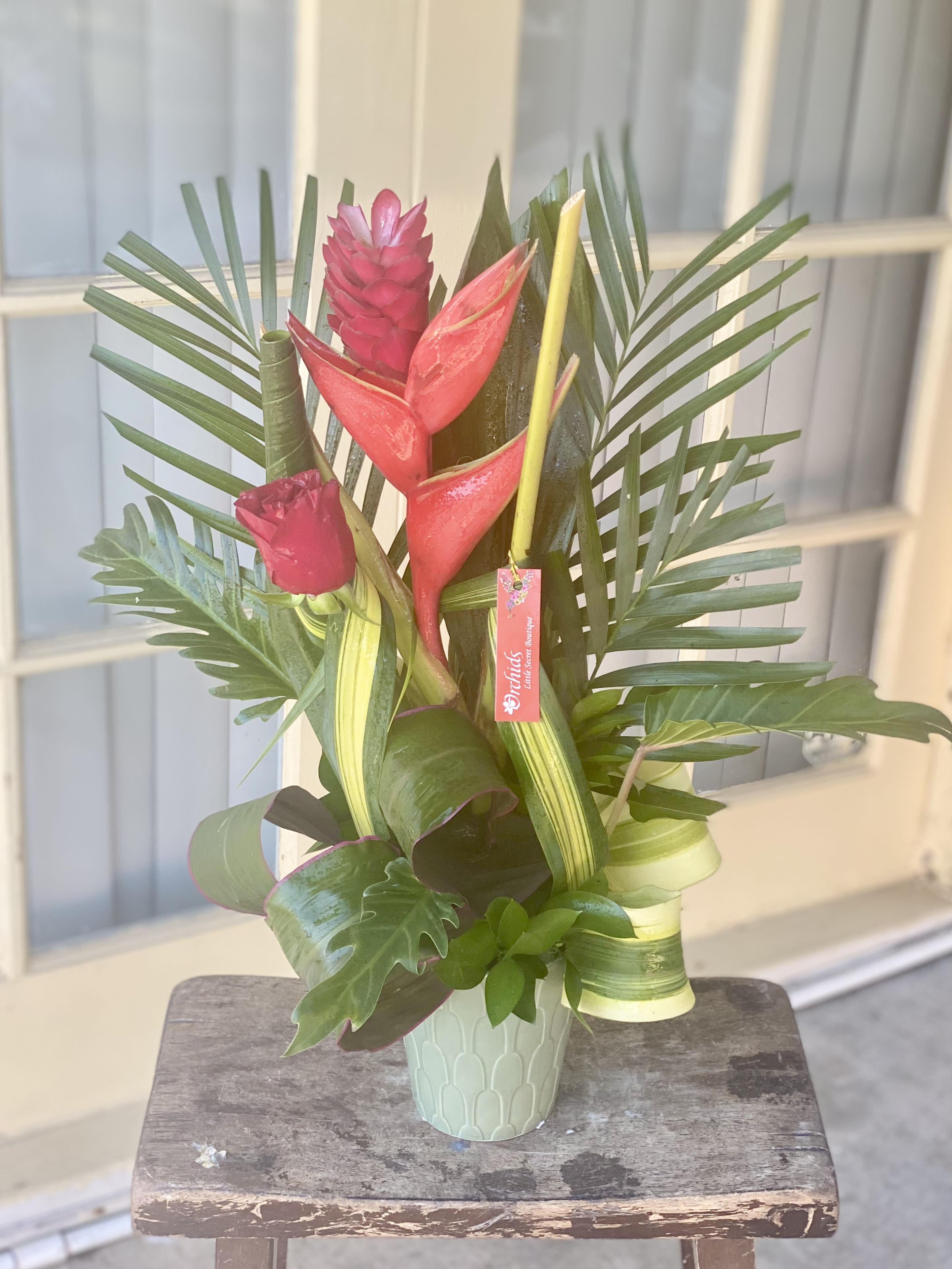 Tropical arrangement with red heliconia and palm leaves in a mint vase