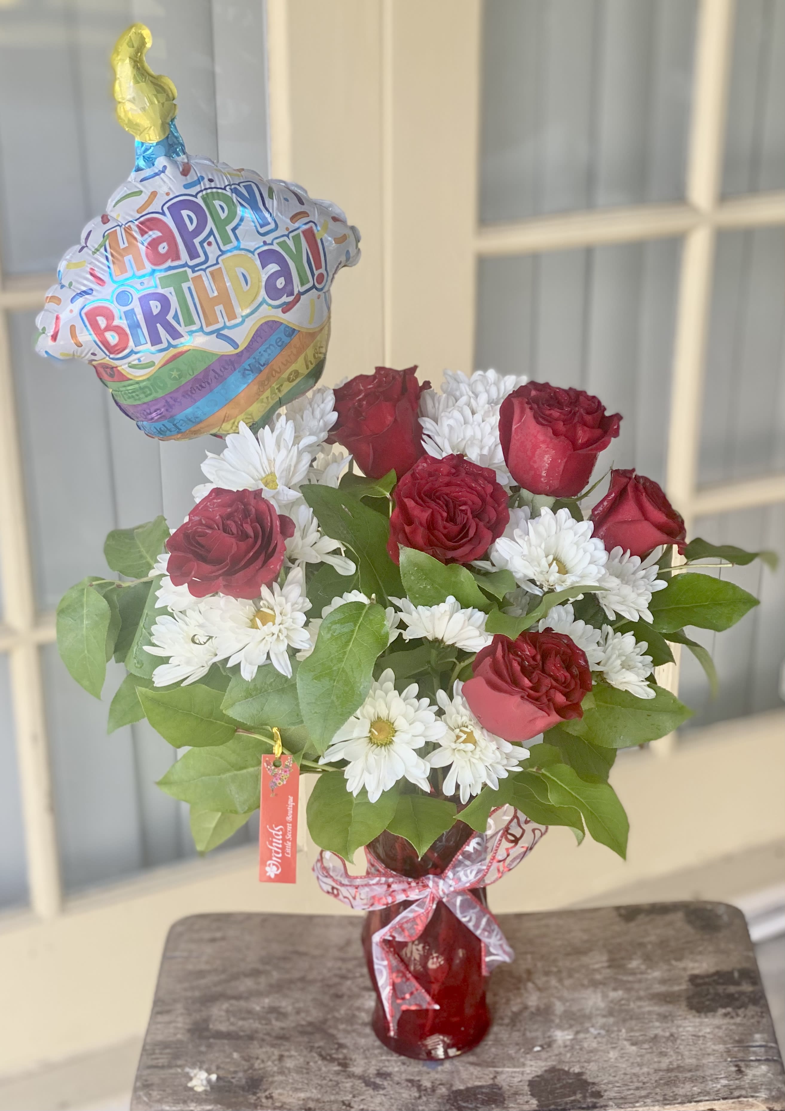 Red roses and white daisies in a vase with a birthday balloon