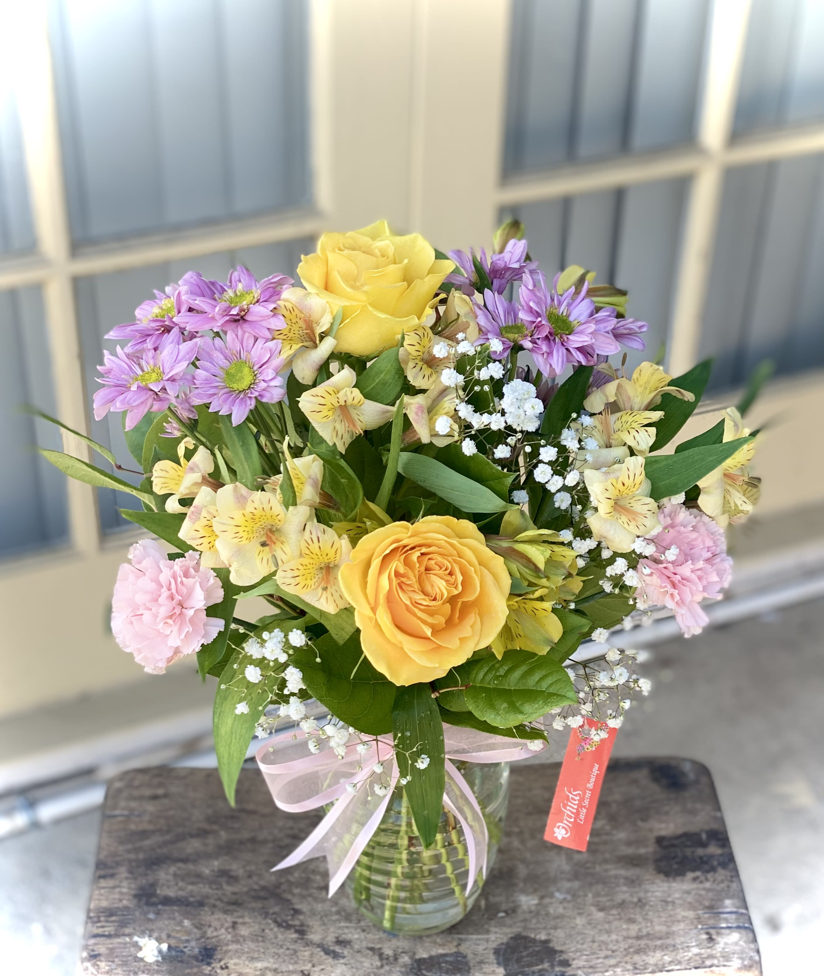 Bouquet of yellow roses, purple daisies, and pink carnations in a glass vase