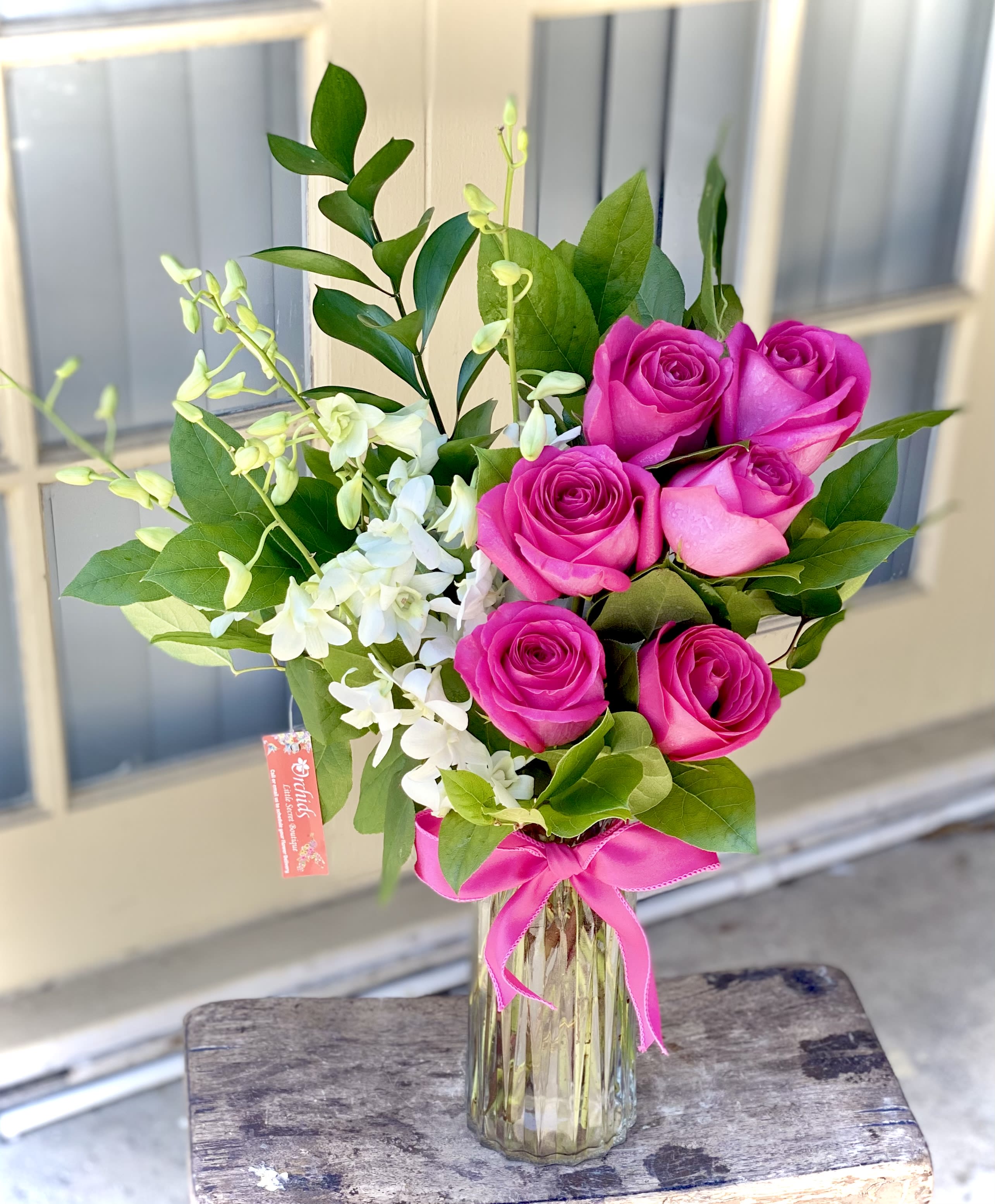 Pink roses and white orchids in a glass vase with a pink ribbon