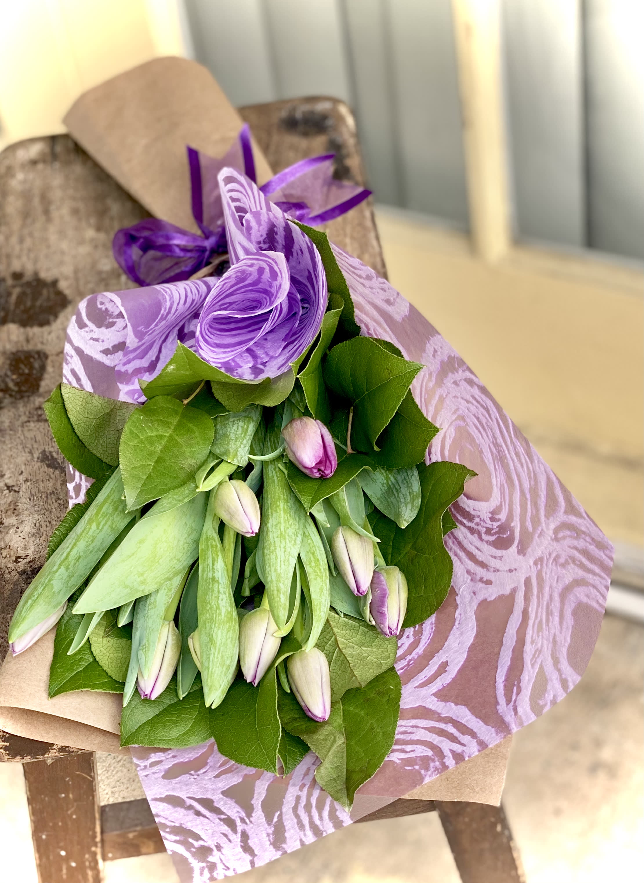 Purple-wrapped bouquet of pale tulips with green leaves