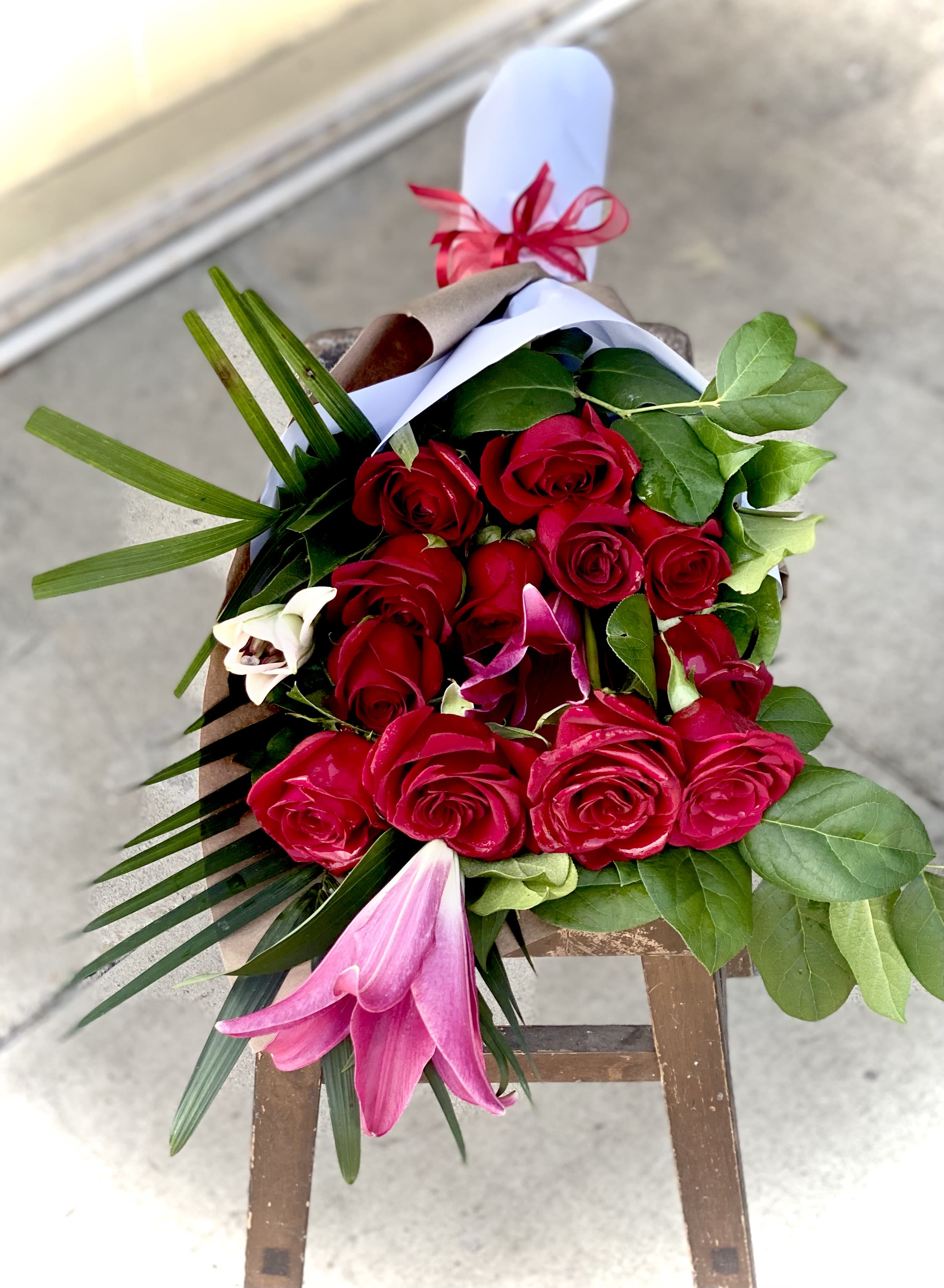Bouquet of red roses with pink lilies and greenery wrapped in paper