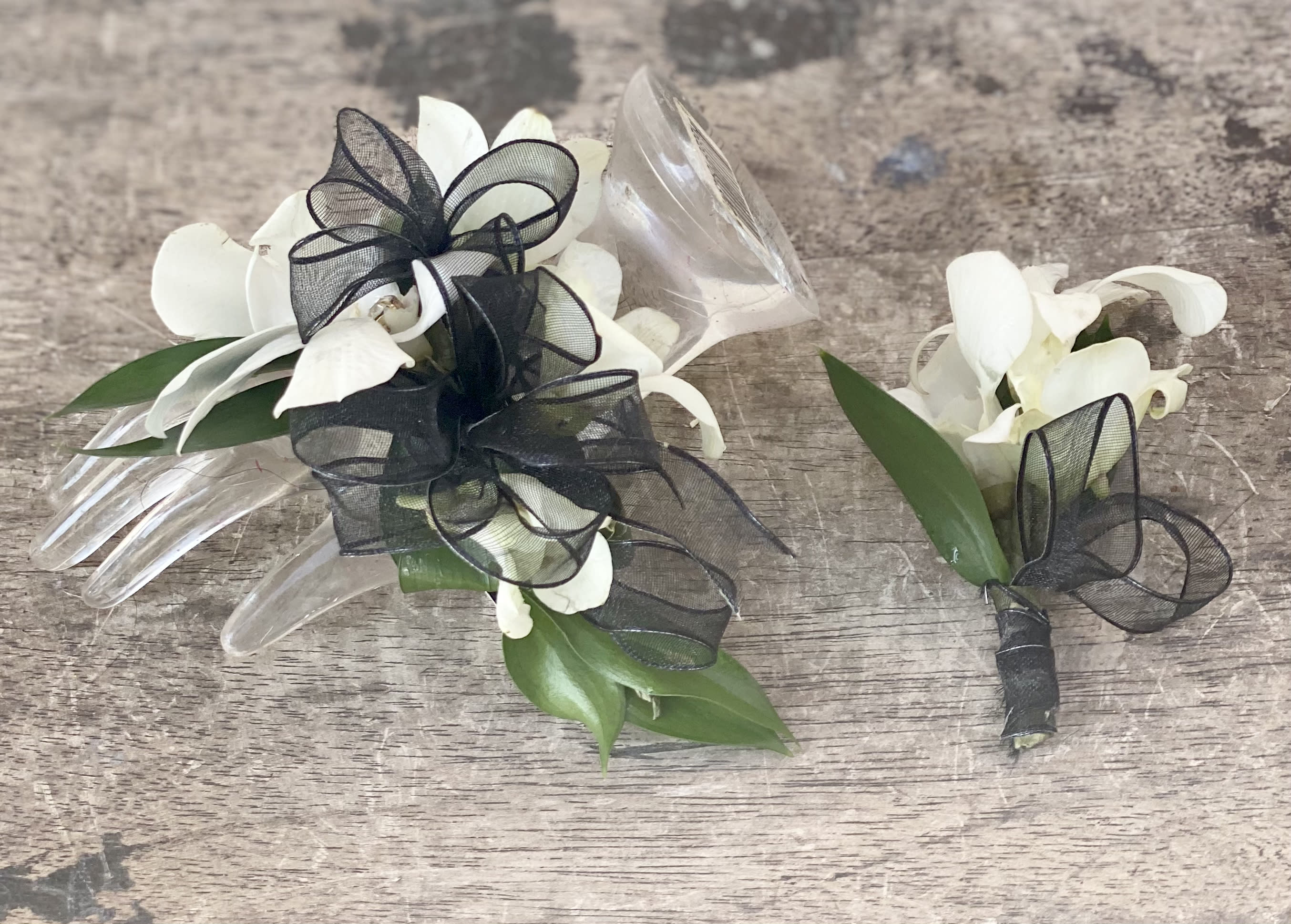 White orchid corsages with black ribbon bows on a wood surface
