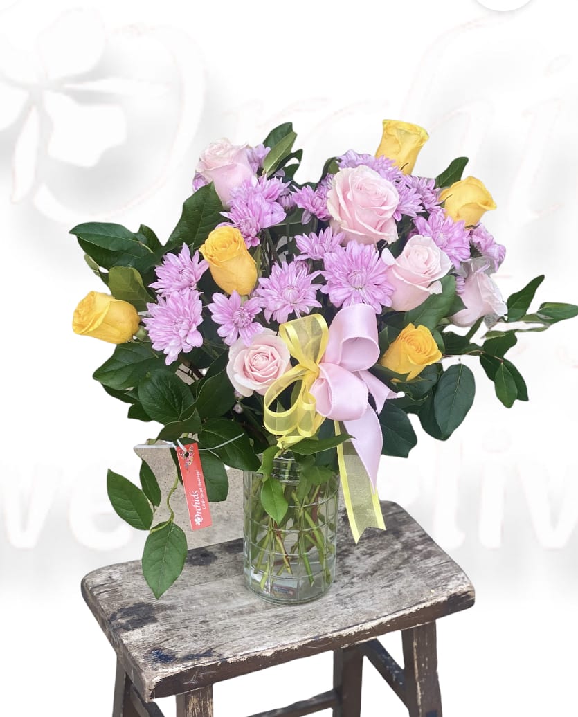 Pink and yellow roses with lavender daisies in a glass vase