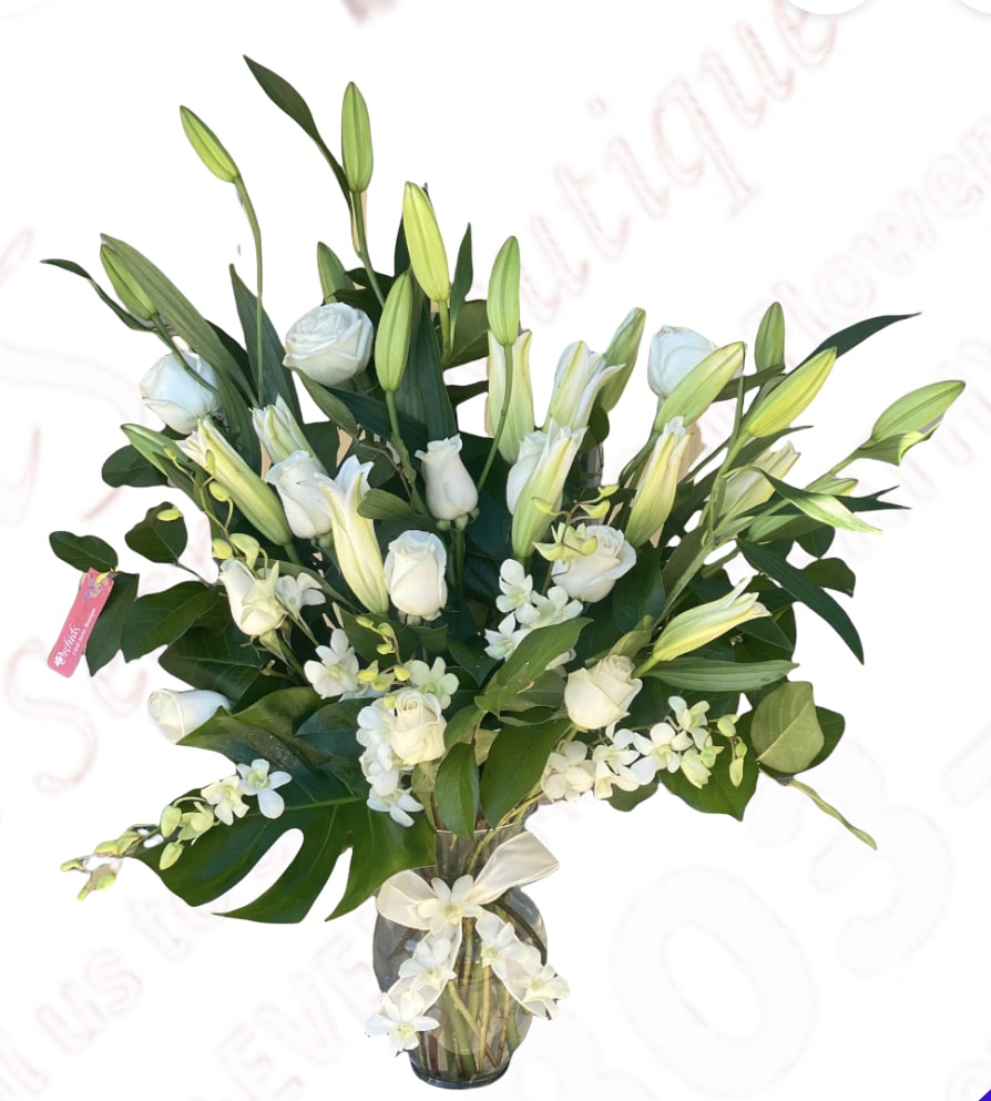 White roses and lilies in a glass vase with greenery