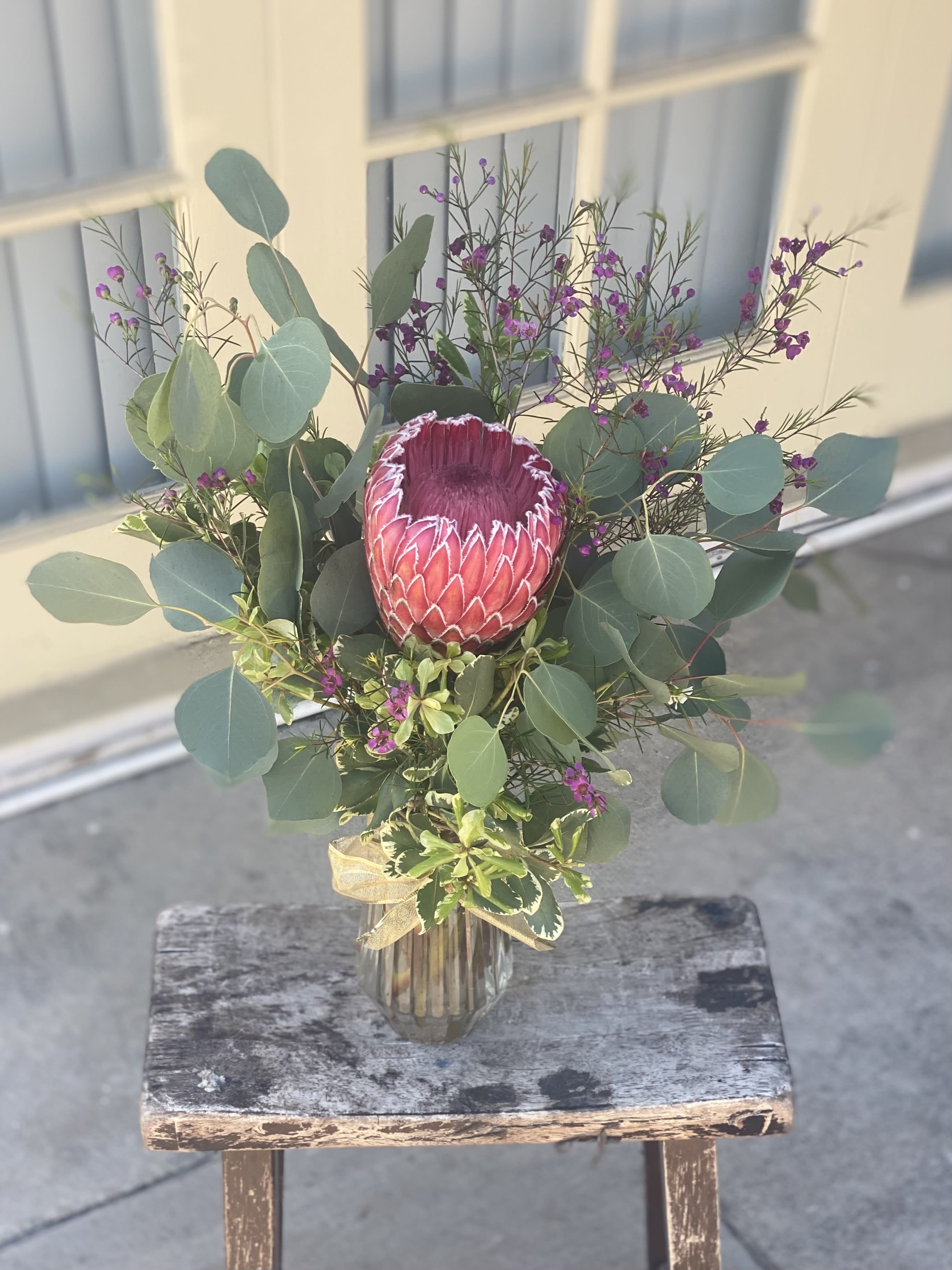 Protea bouquet in a glass vase with eucalyptus and purple filler flowers