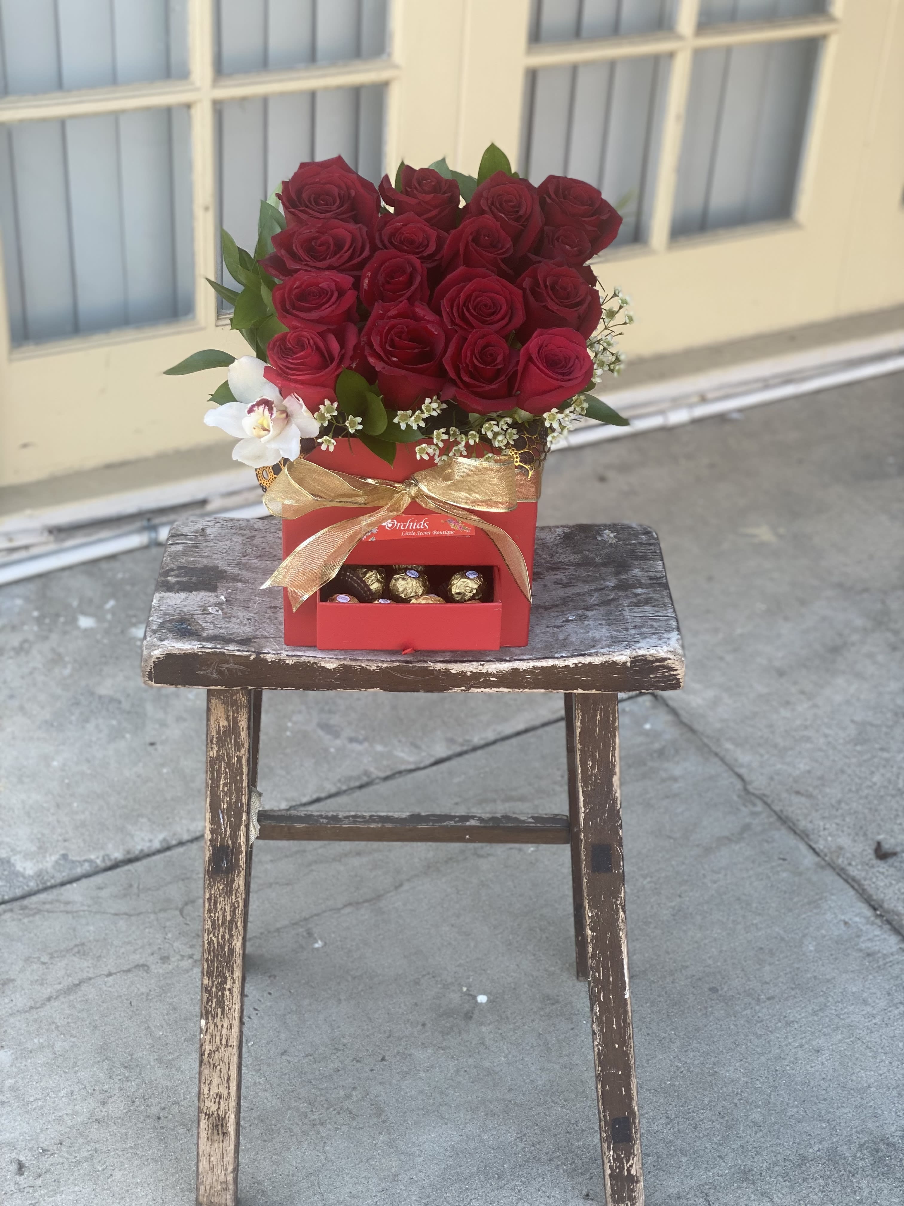 Red rose arrangement in a red gift box with chocolates and a gold ribbon
