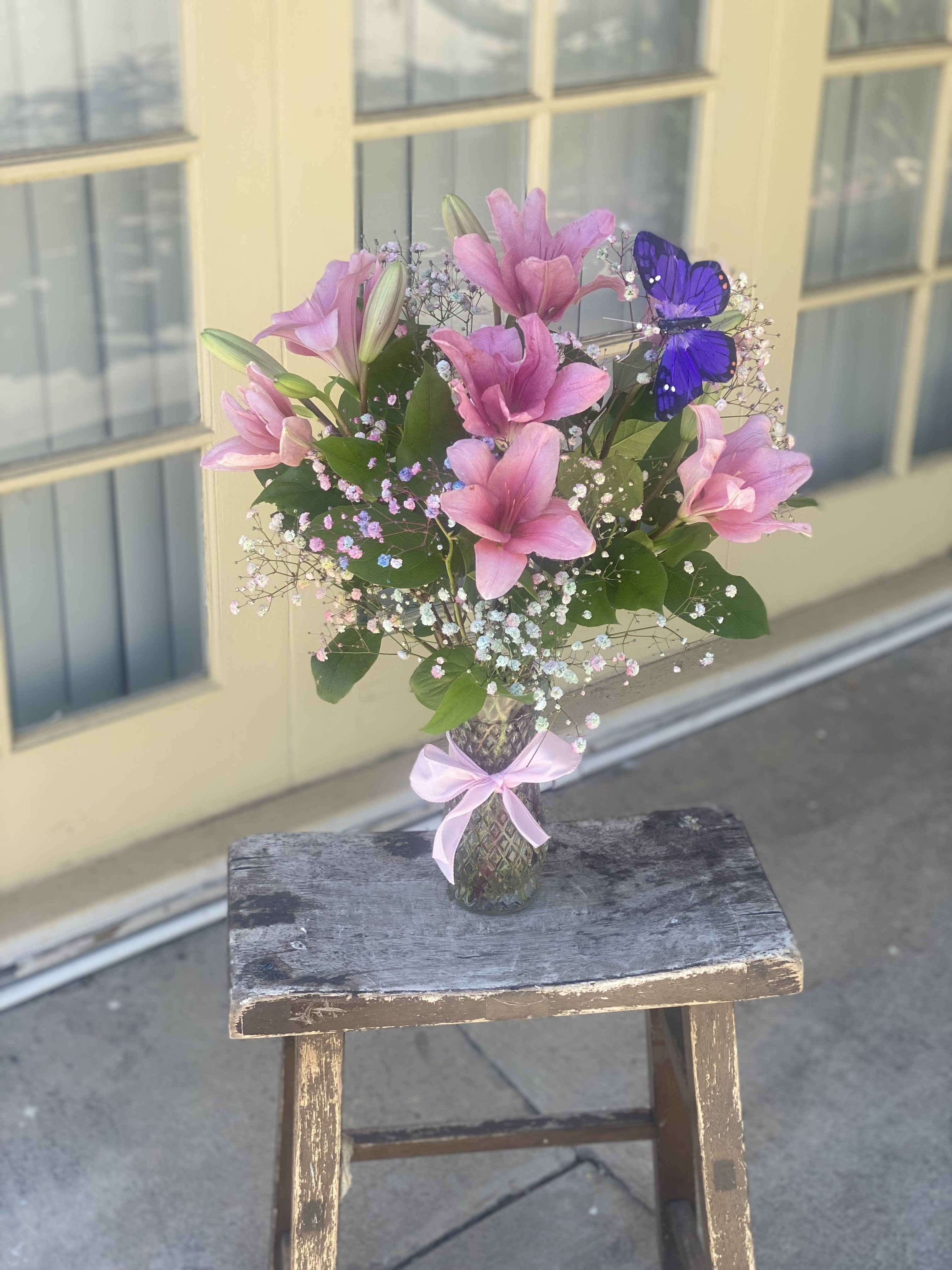 Pink lilies in a glass vase with a purple butterfly decoration