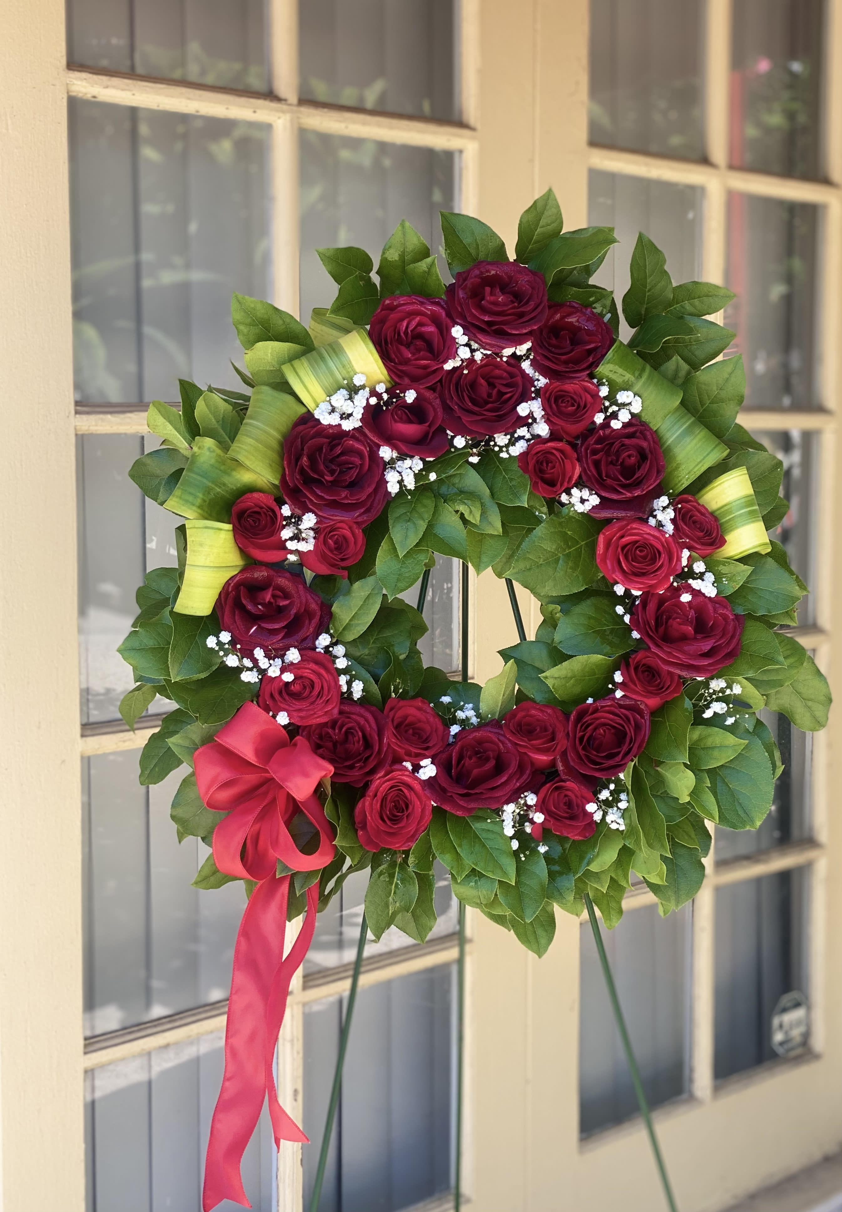 Circular wreath of red roses with white baby's breath and a pink ribbon