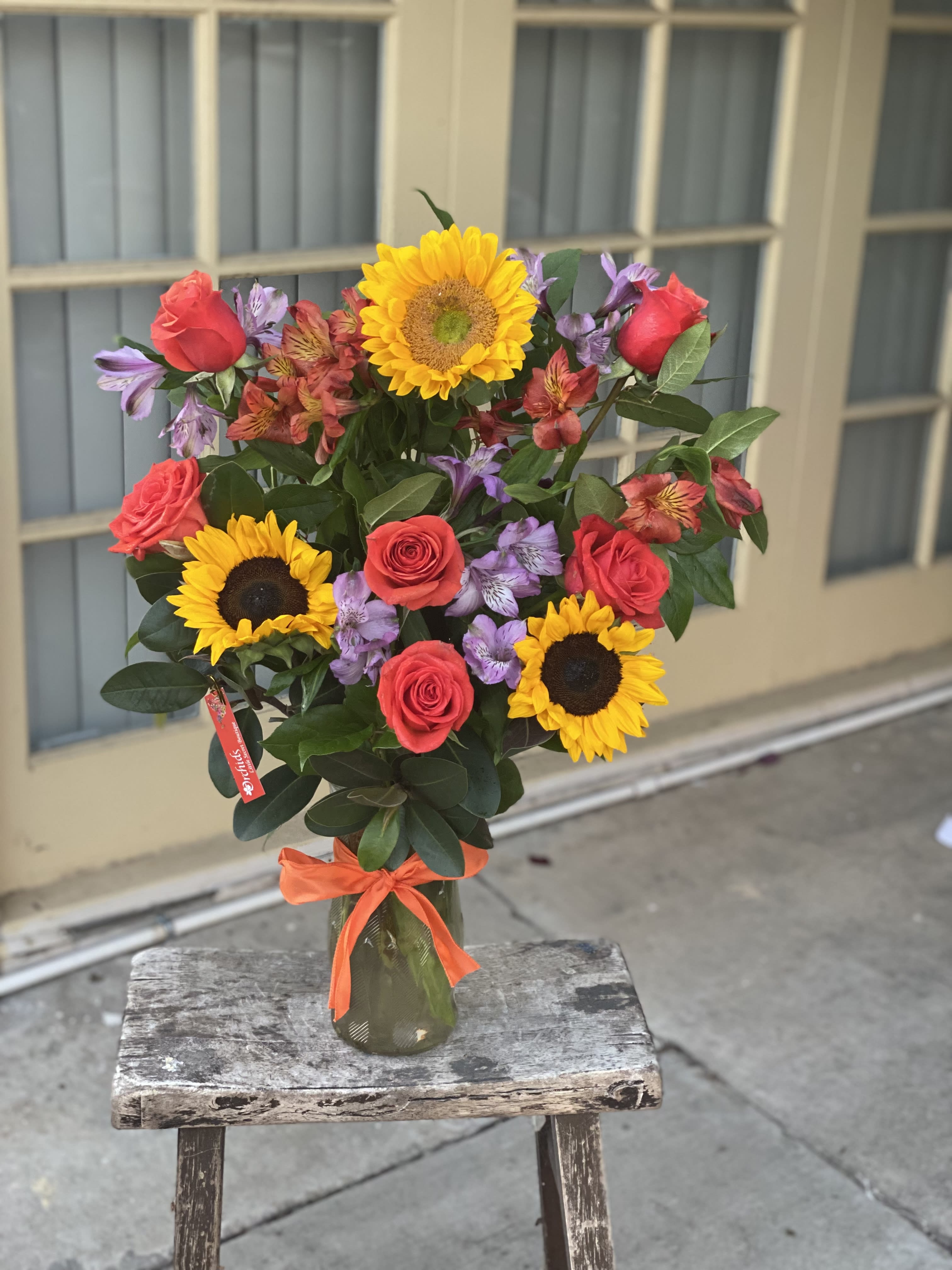 Bouquet of sunflowers, red roses, and purple alstroemeria in a glass vase
