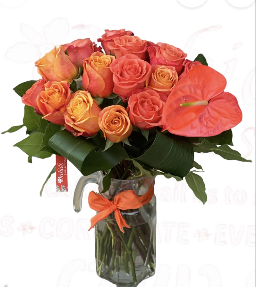 Bouquet of orange and coral roses in a glass pitcher vase