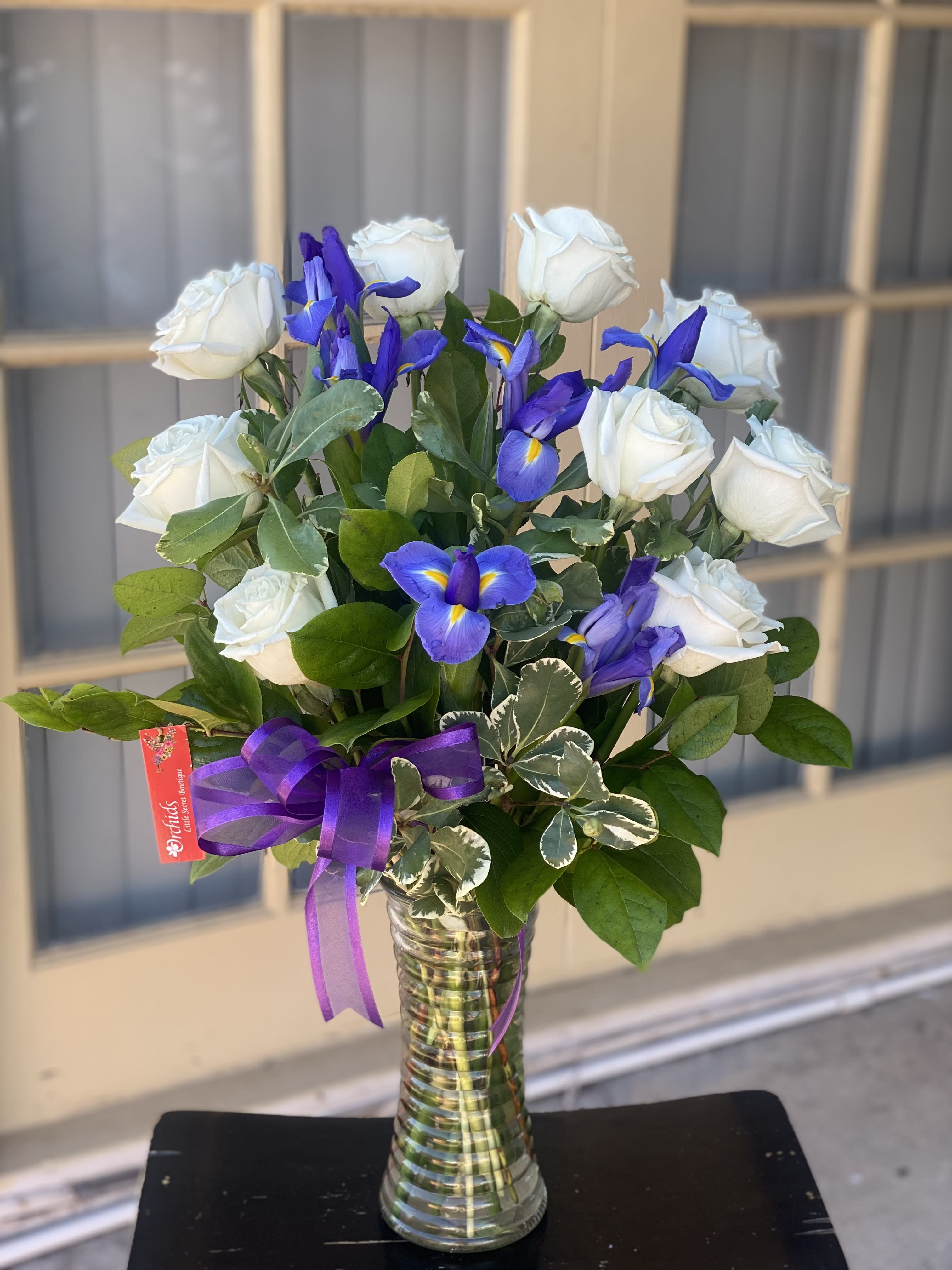 White roses and blue irises in a glass vase with a purple ribbon