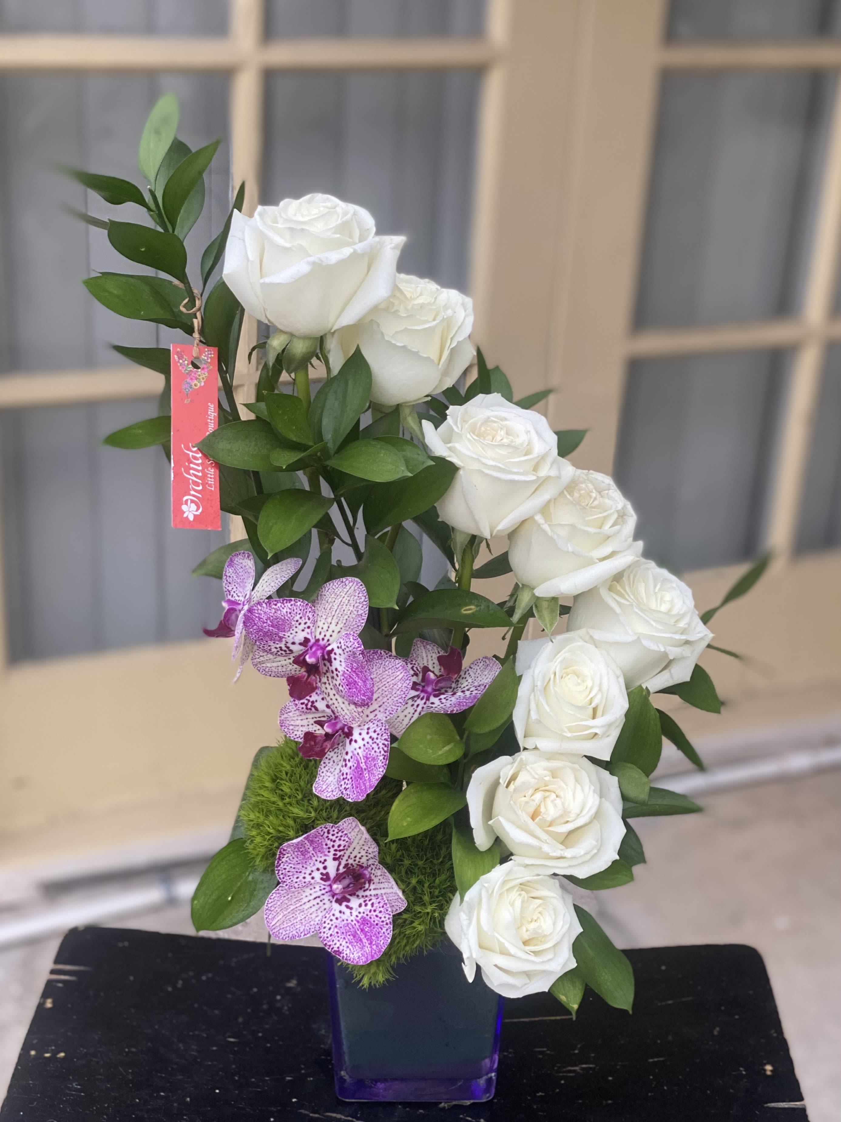 White roses and purple orchids in a square vase