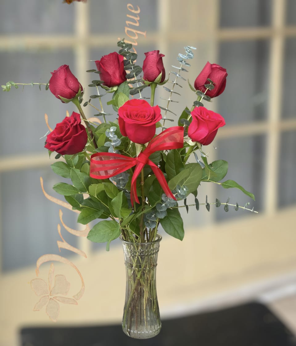 Red roses arranged in a clear glass vase with a red ribbon