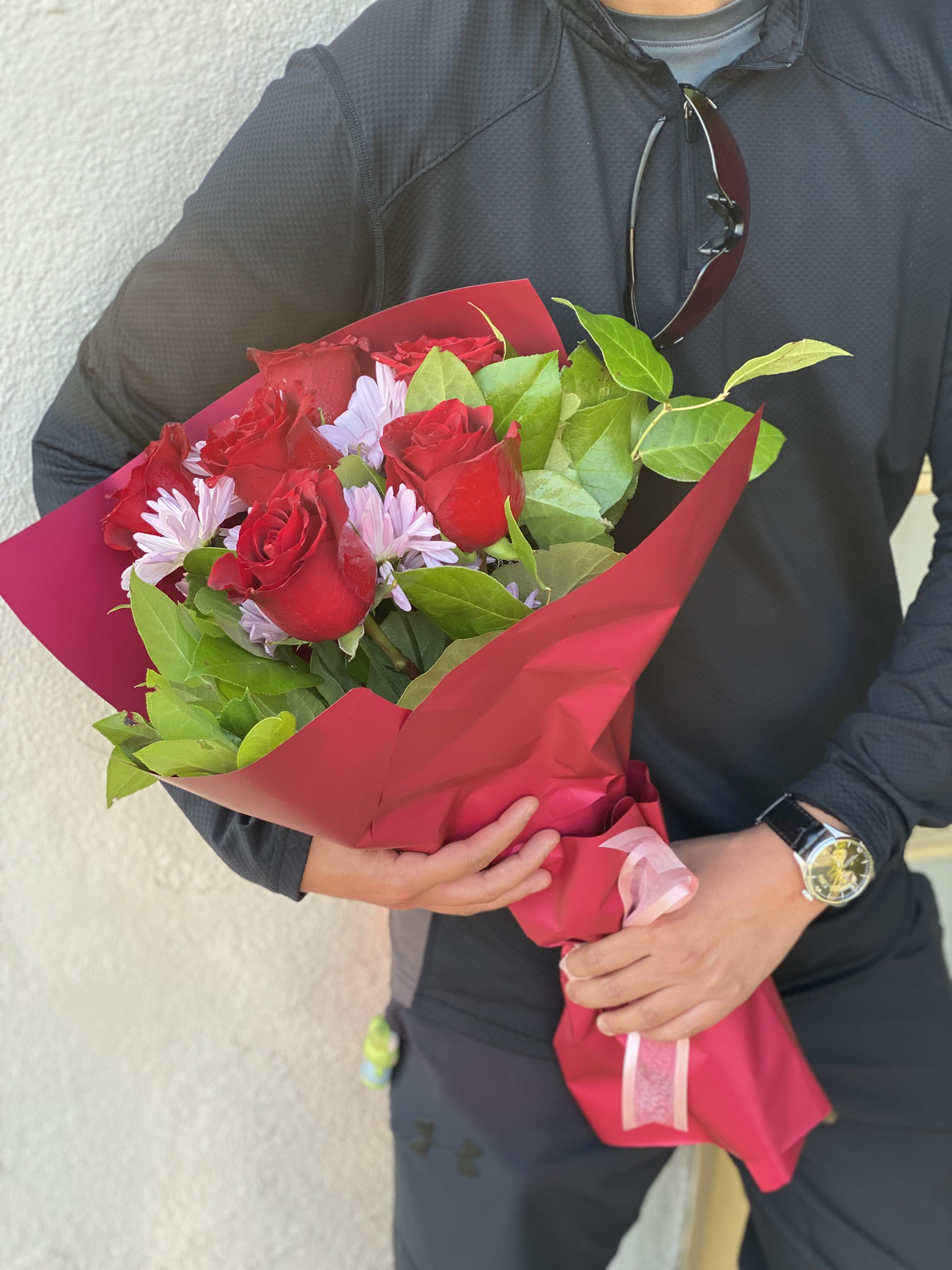 Bouquet of red roses and pale purple daisies wrapped in pink paper