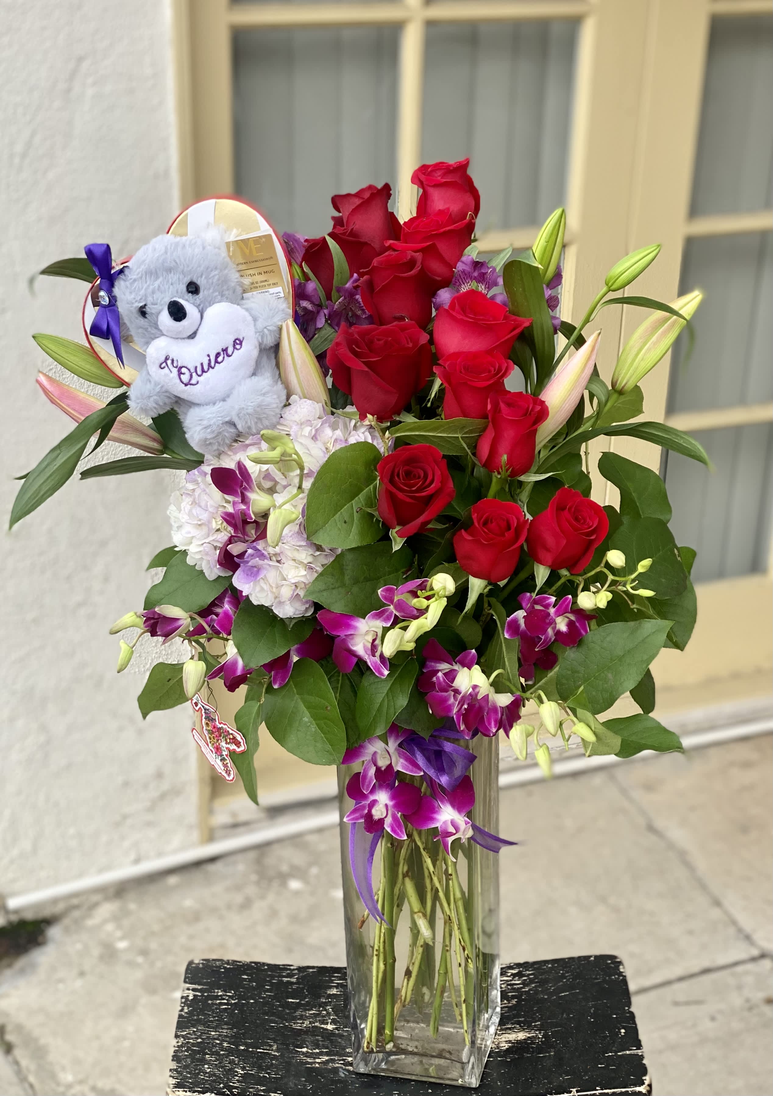 Red roses and purple orchids in a clear vase with a teddy bear