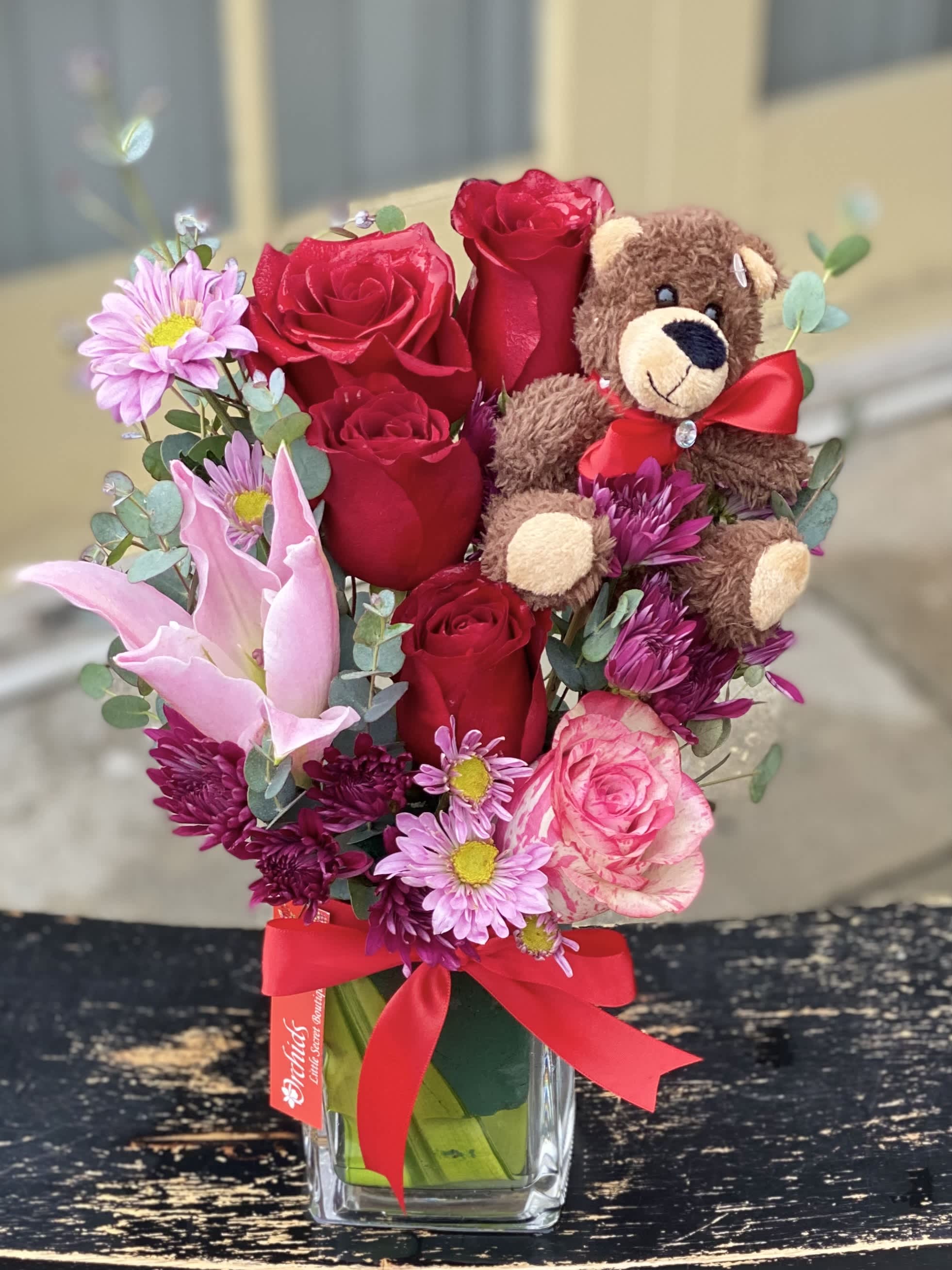 Bouquet of red roses and pink flowers with a teddy bear in a glass vase