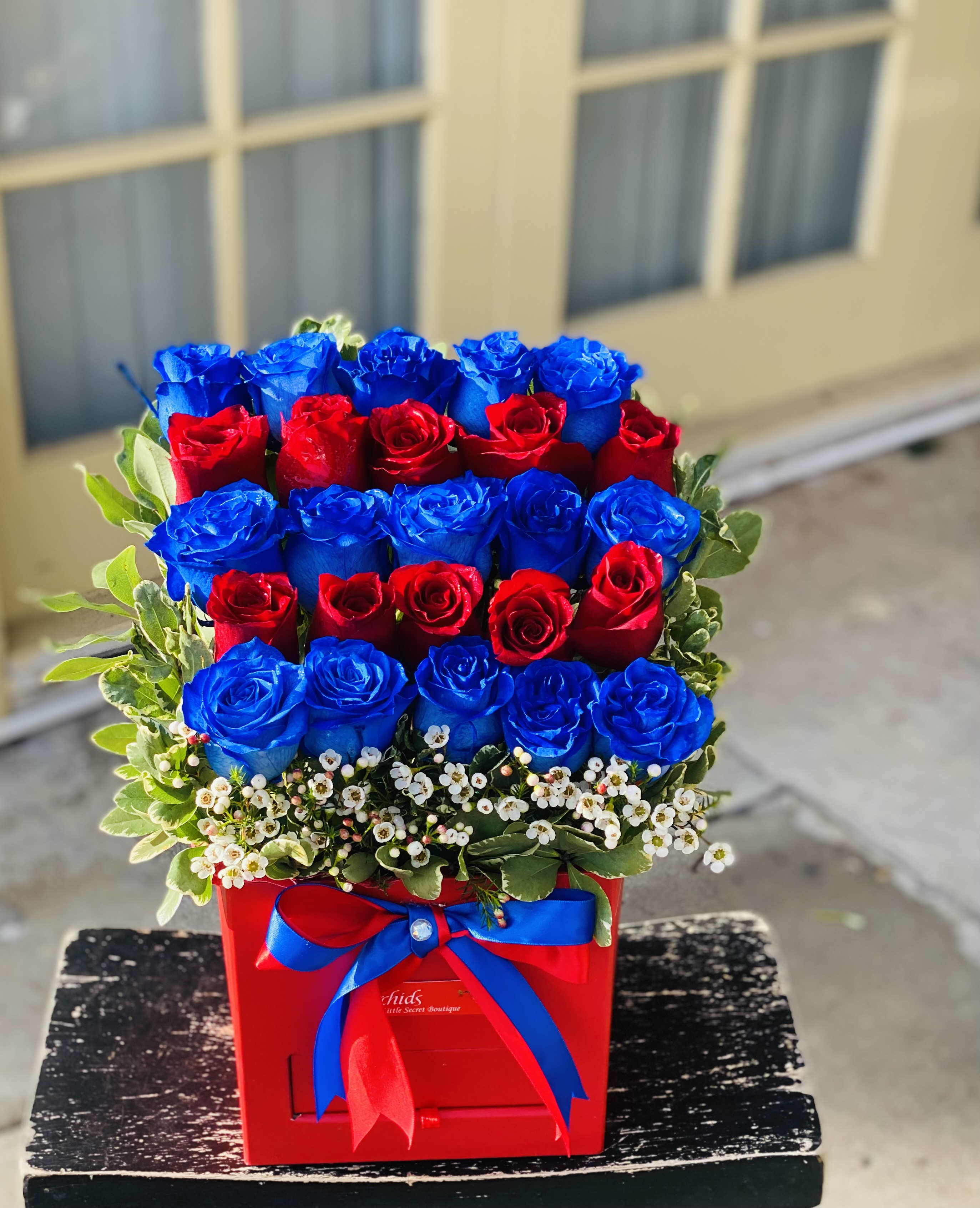 Red and blue roses arranged in a red box with a ribbon