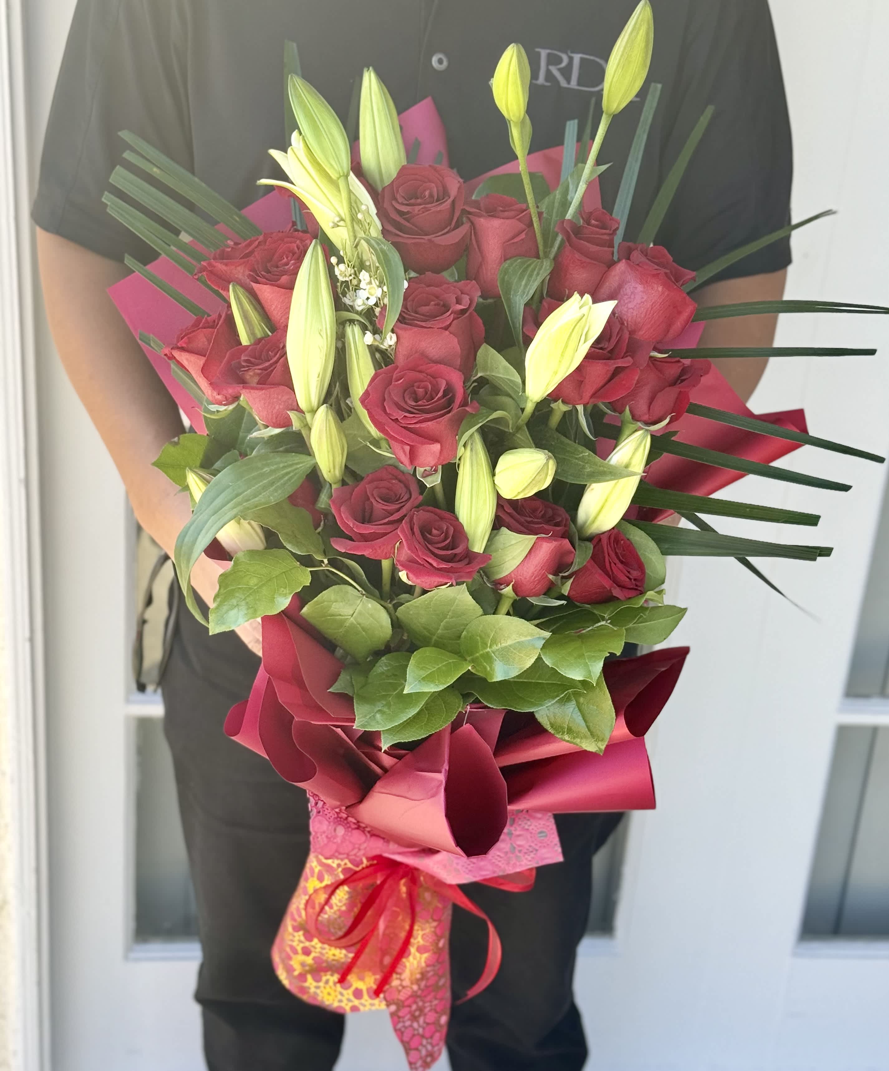 Bouquet of red roses and yellow lily buds wrapped in pink paper