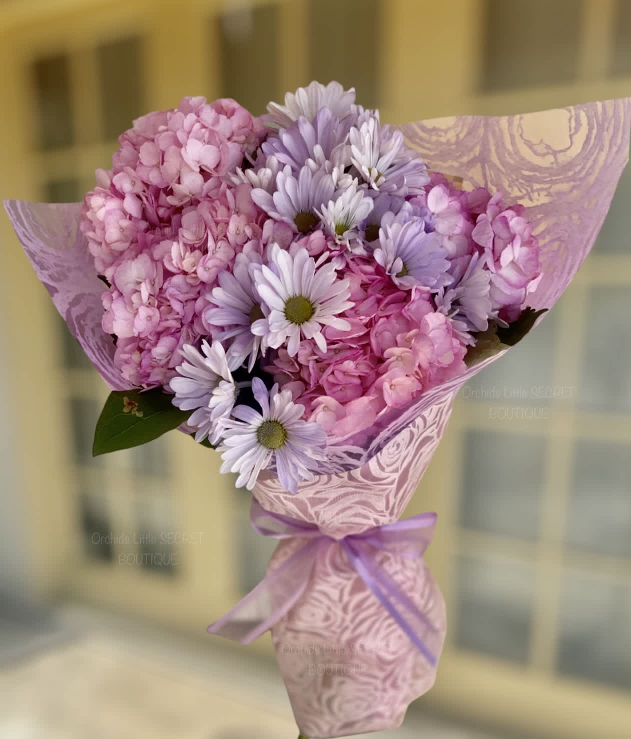 Pink and lavender bouquet wrapped in patterned paper with a ribbon