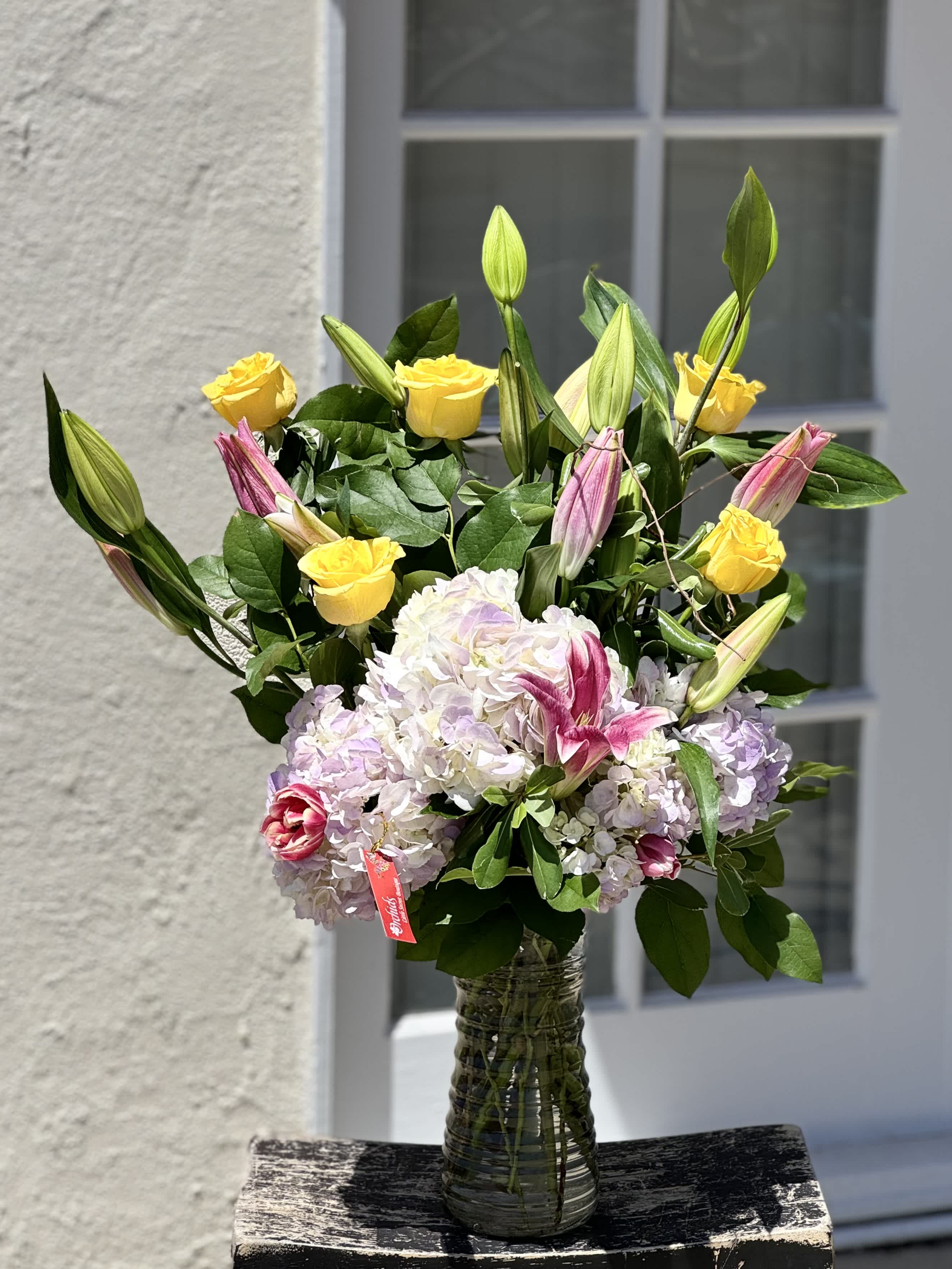 Bouquet of yellow roses, pink lilies, and pale hydrangeas in a glass vase
