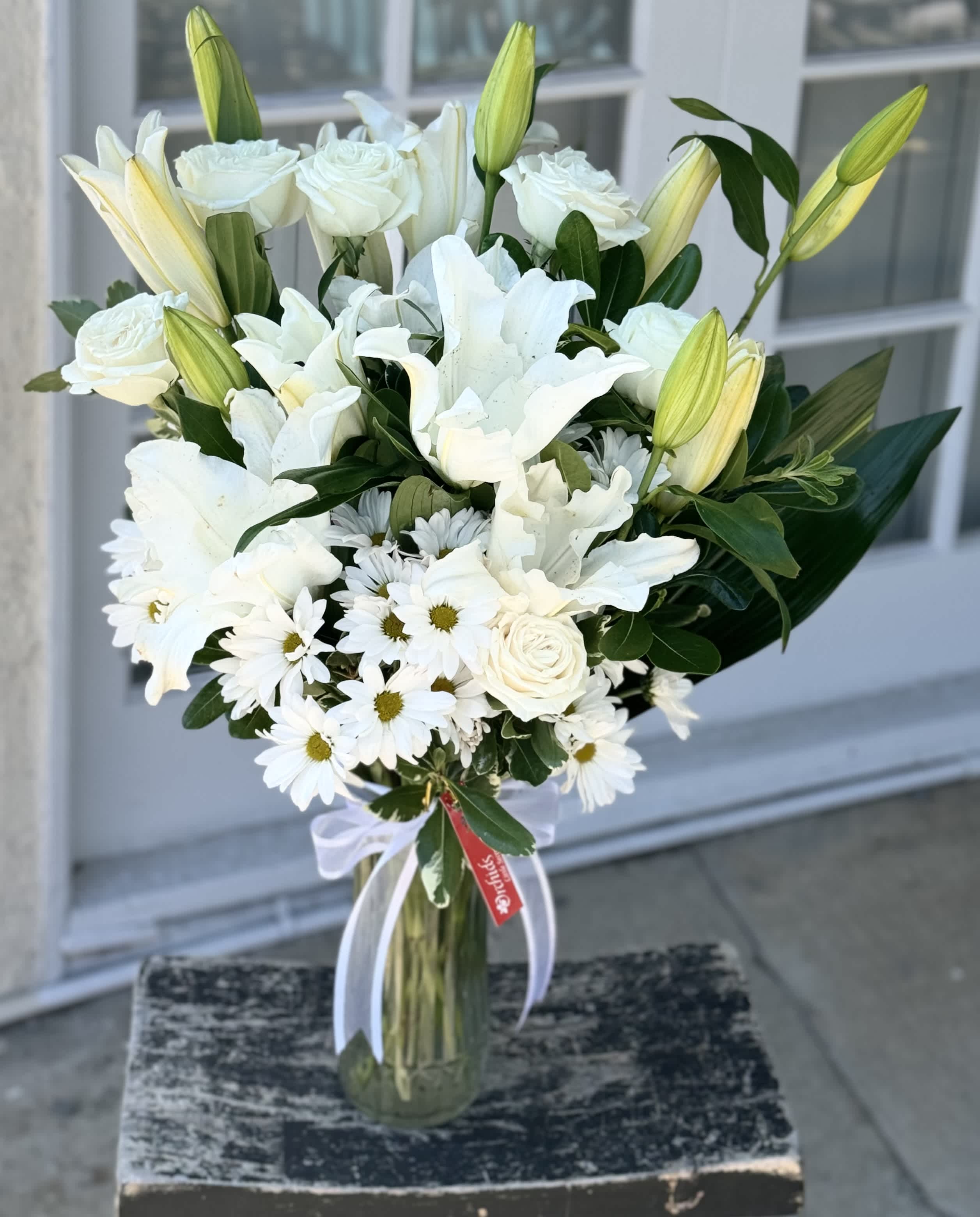 White lilies, roses, and daisies in a glass vase