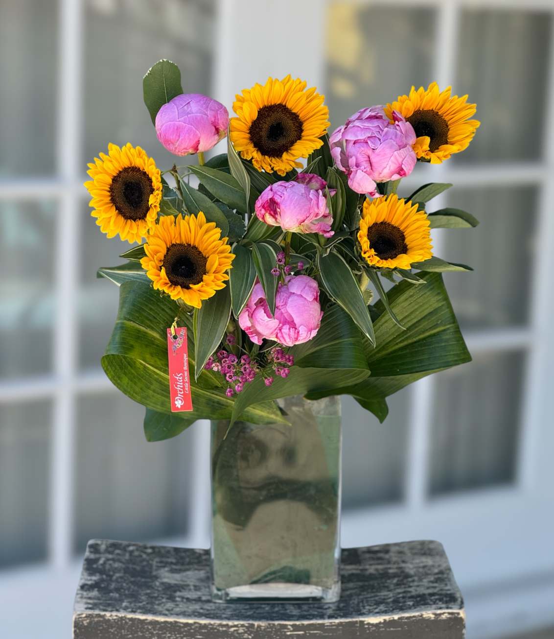 Sunflowers and pink peonies arranged in a tall glass vase